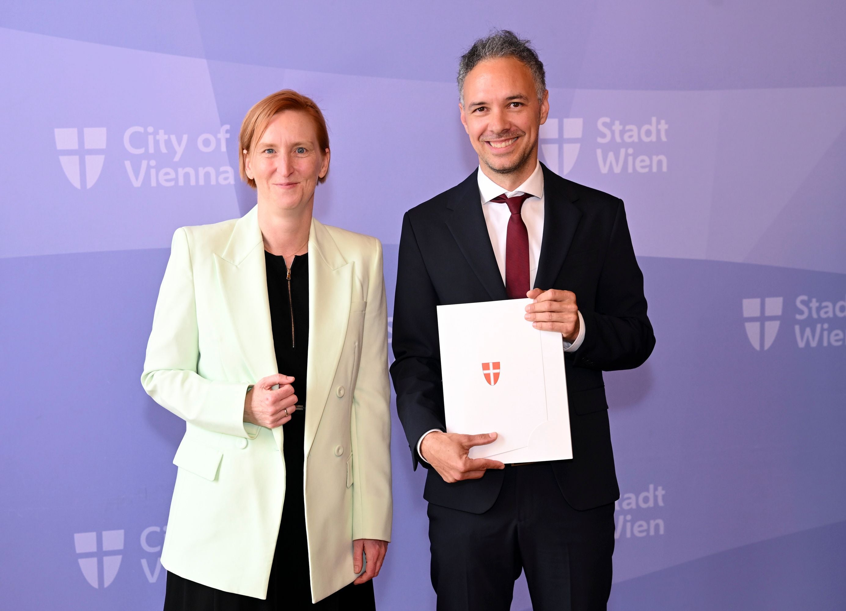 Elke Hanel-Torsch und Ilja Messner stehen vor einer Wand mit "Stadt Wien"-Logo.