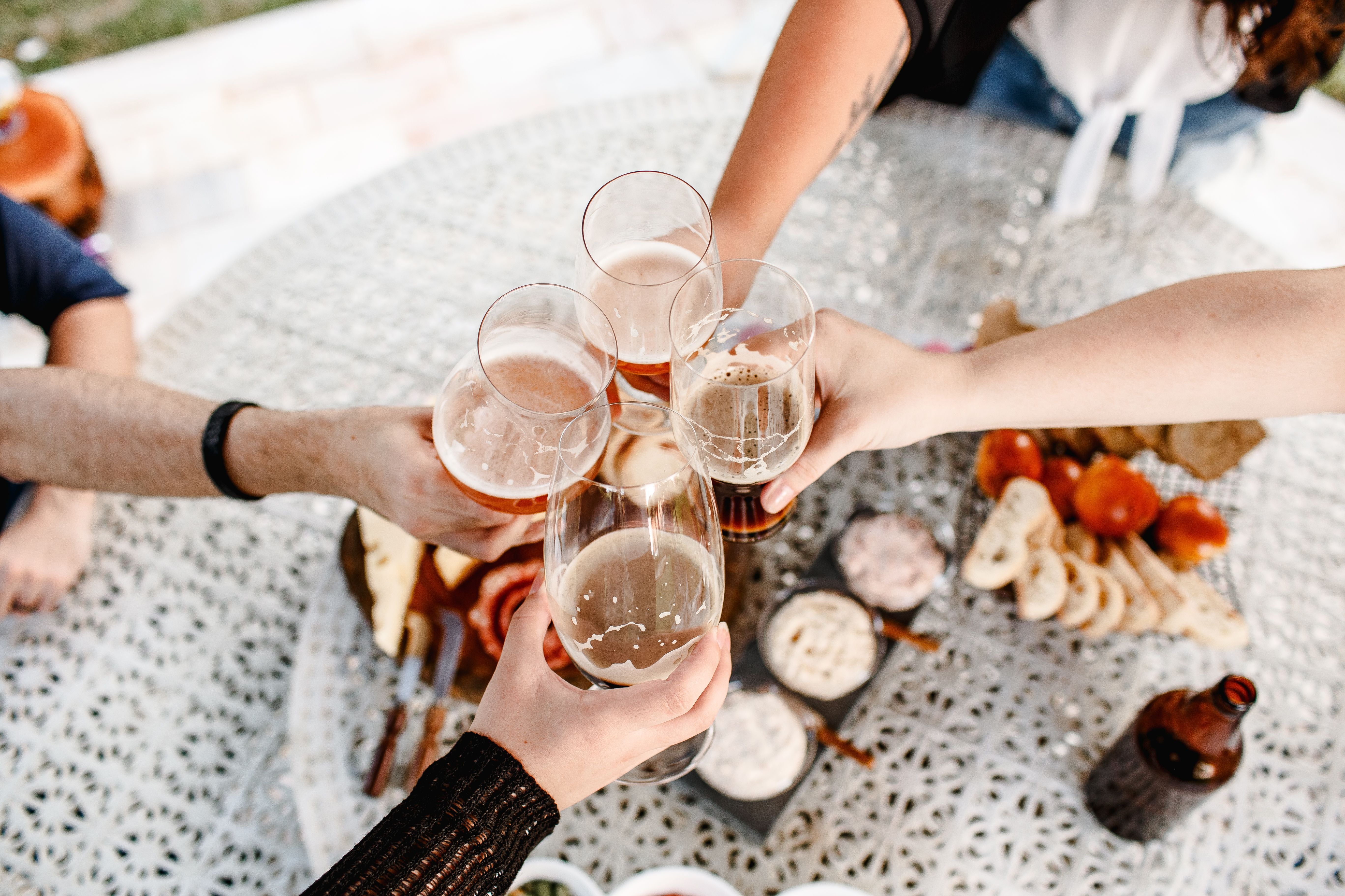 Vier Personen stoßen mit Biergläsern an einem Tisch mit Snacks und Dips an.