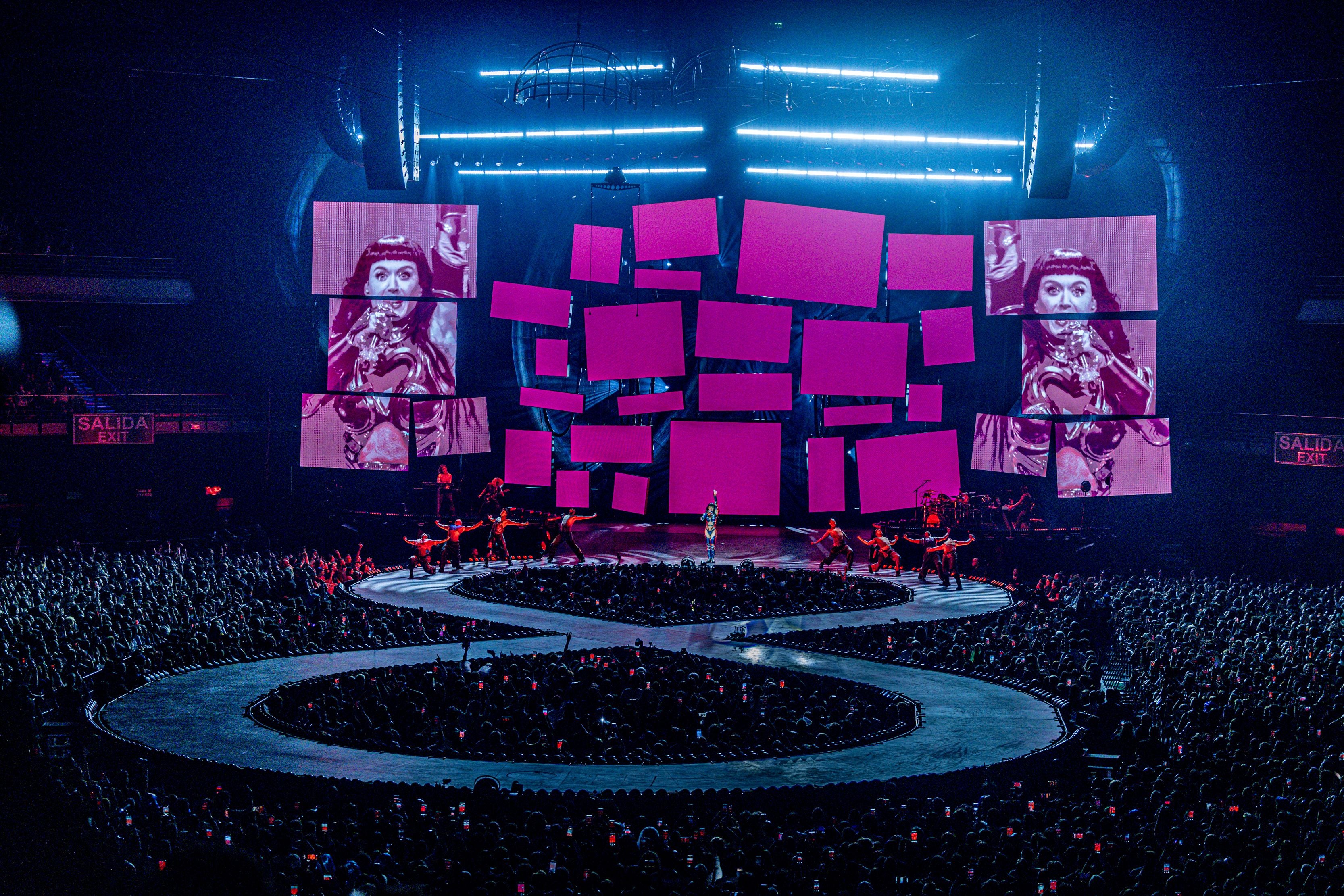 Katy Perry singt auf einer großen Bühne mit lila Bildschirmen und tanzenden Darstellern im vollen Stadion.