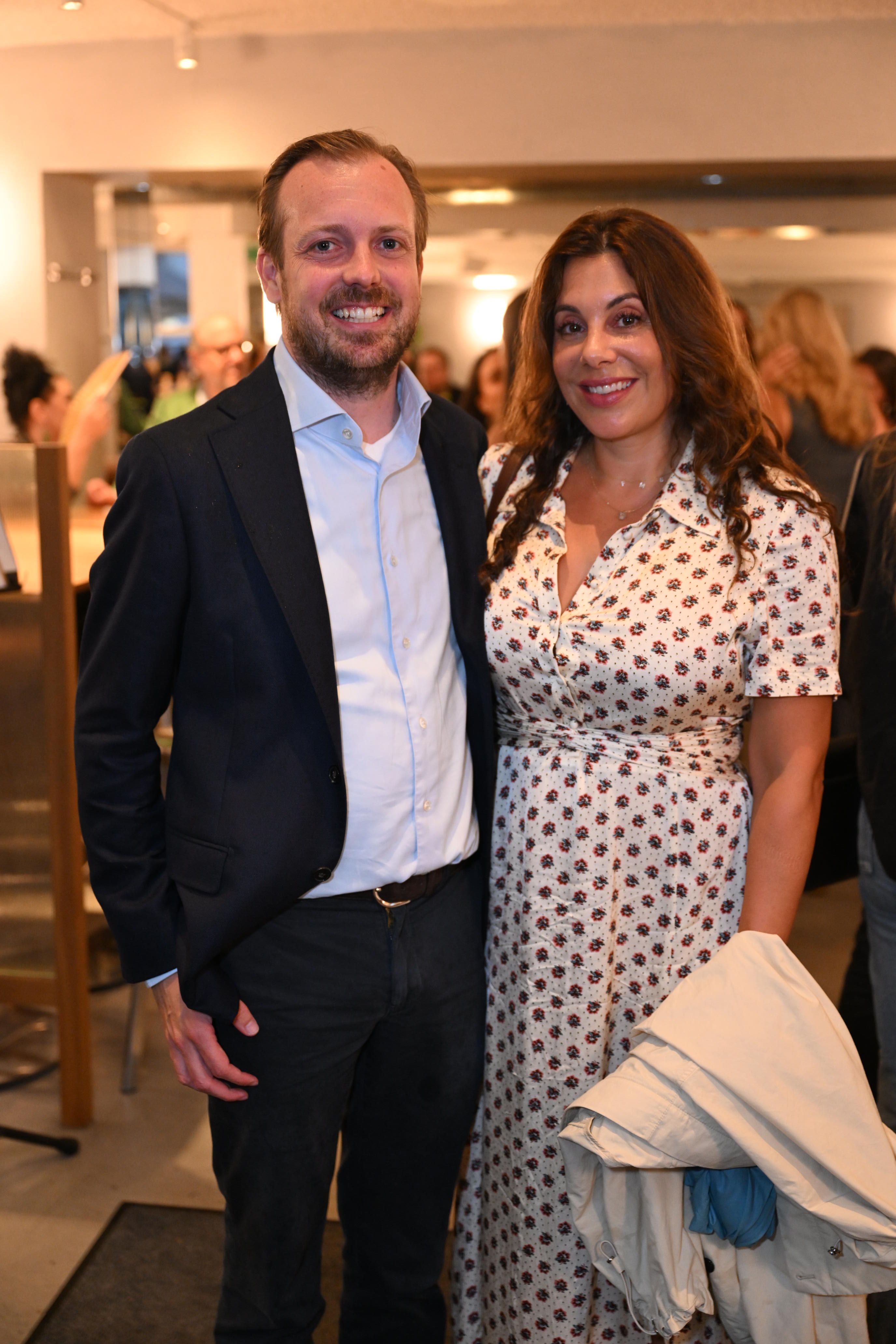 Ein Mann im Anzug und eine Frau im gemusterten Kleid lächeln gemeinsam in die Kamera.