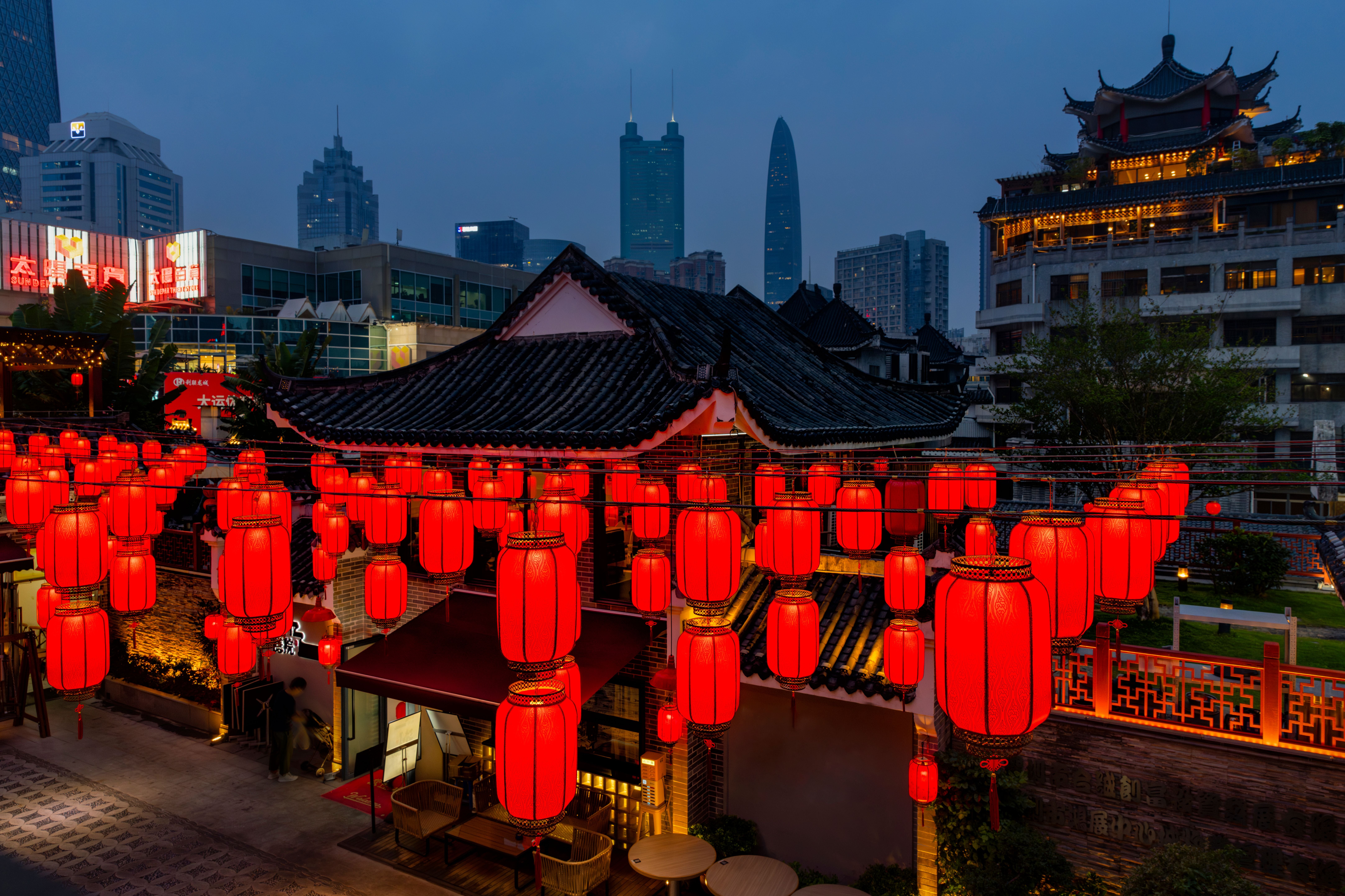 Viele leuchtend rote Laternen vor traditionellen chinesischen Gebäuden mit modernen Hochhäusern dahinter.