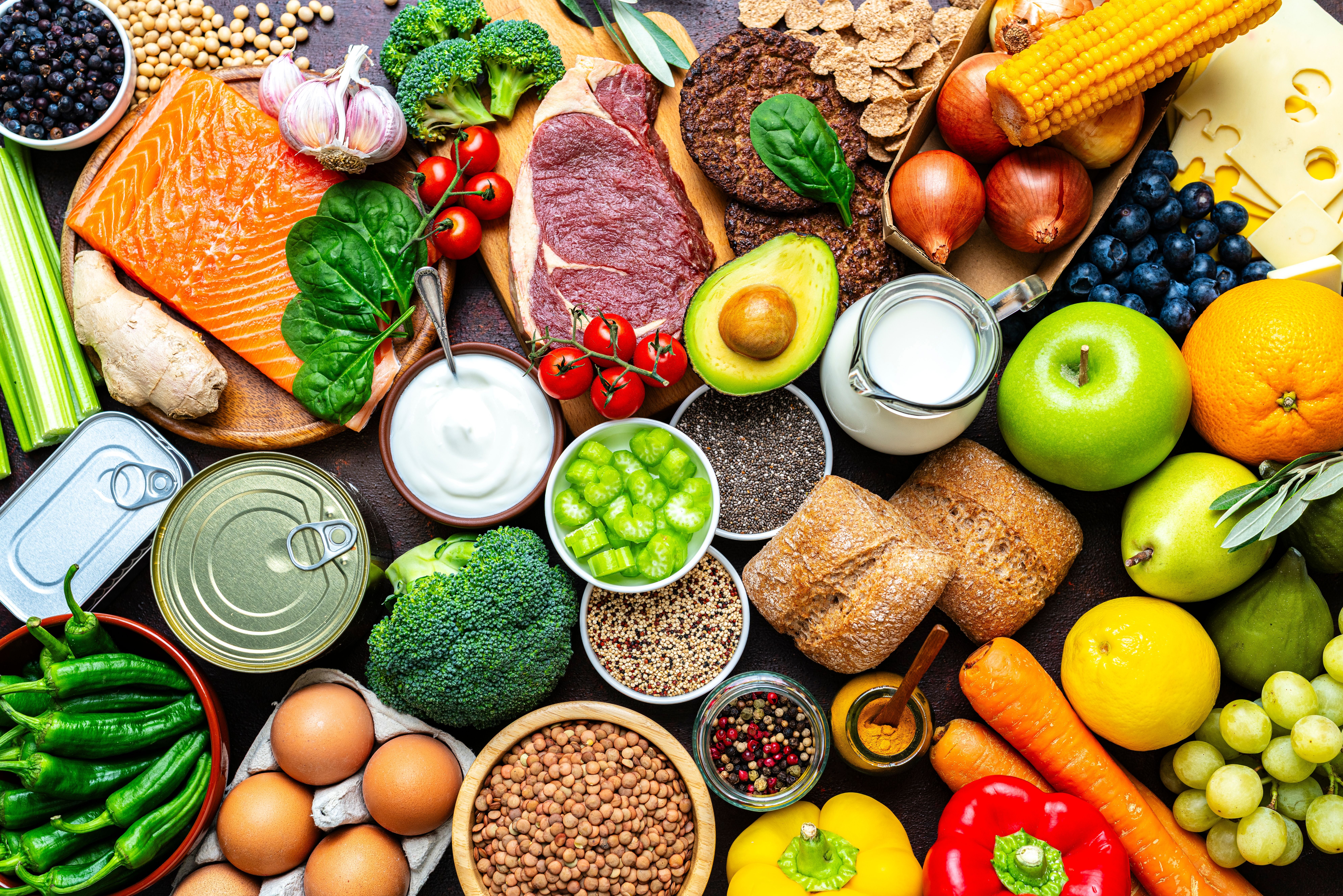 Verschiedene rohe Lebensmittel wie Fleisch, Fisch, Obst, Gemüse, Eier, Milch, Brot und Getreide.
