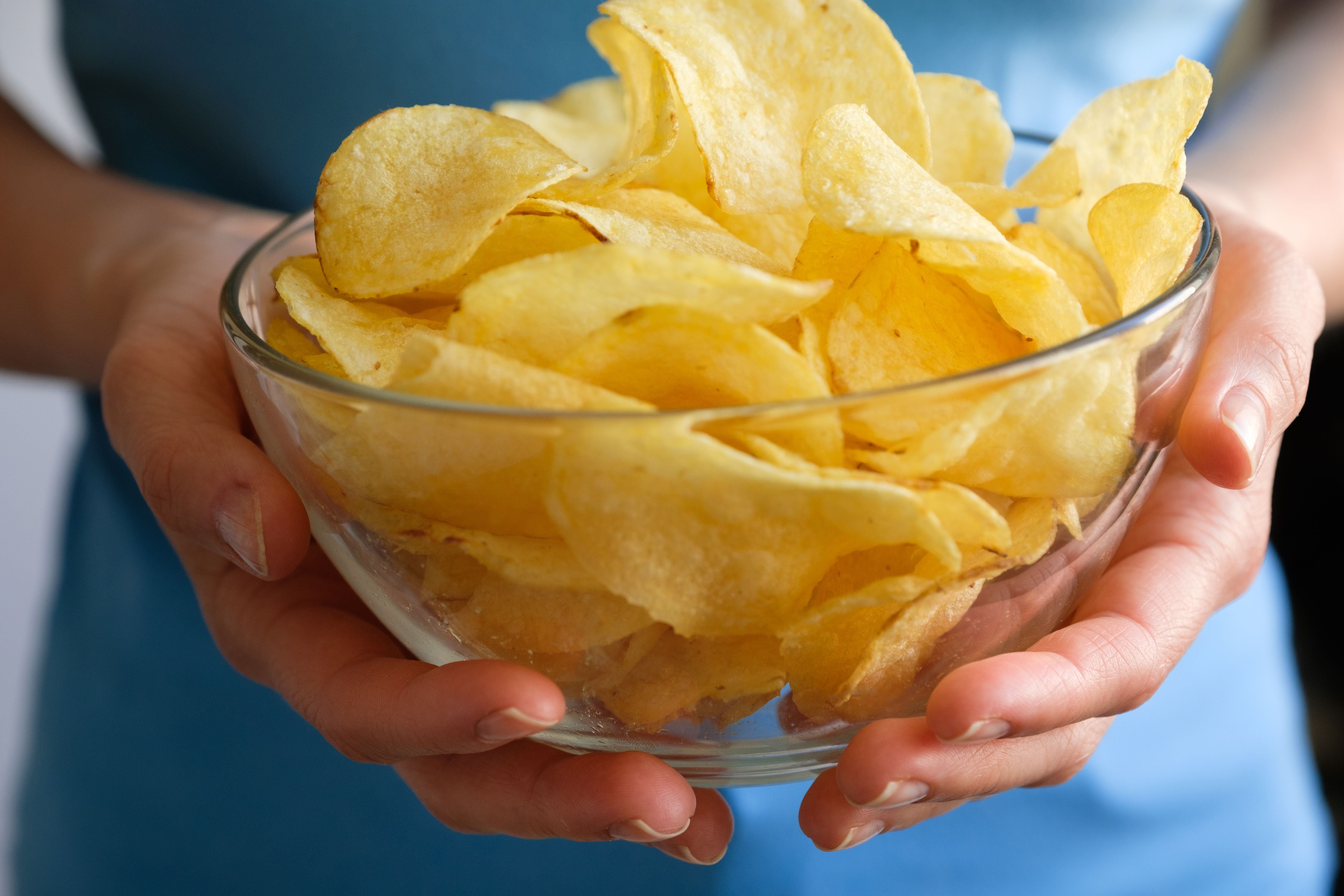 Frau hält eine Glasschale mit knusprigen Kartoffelchips in den Händen.