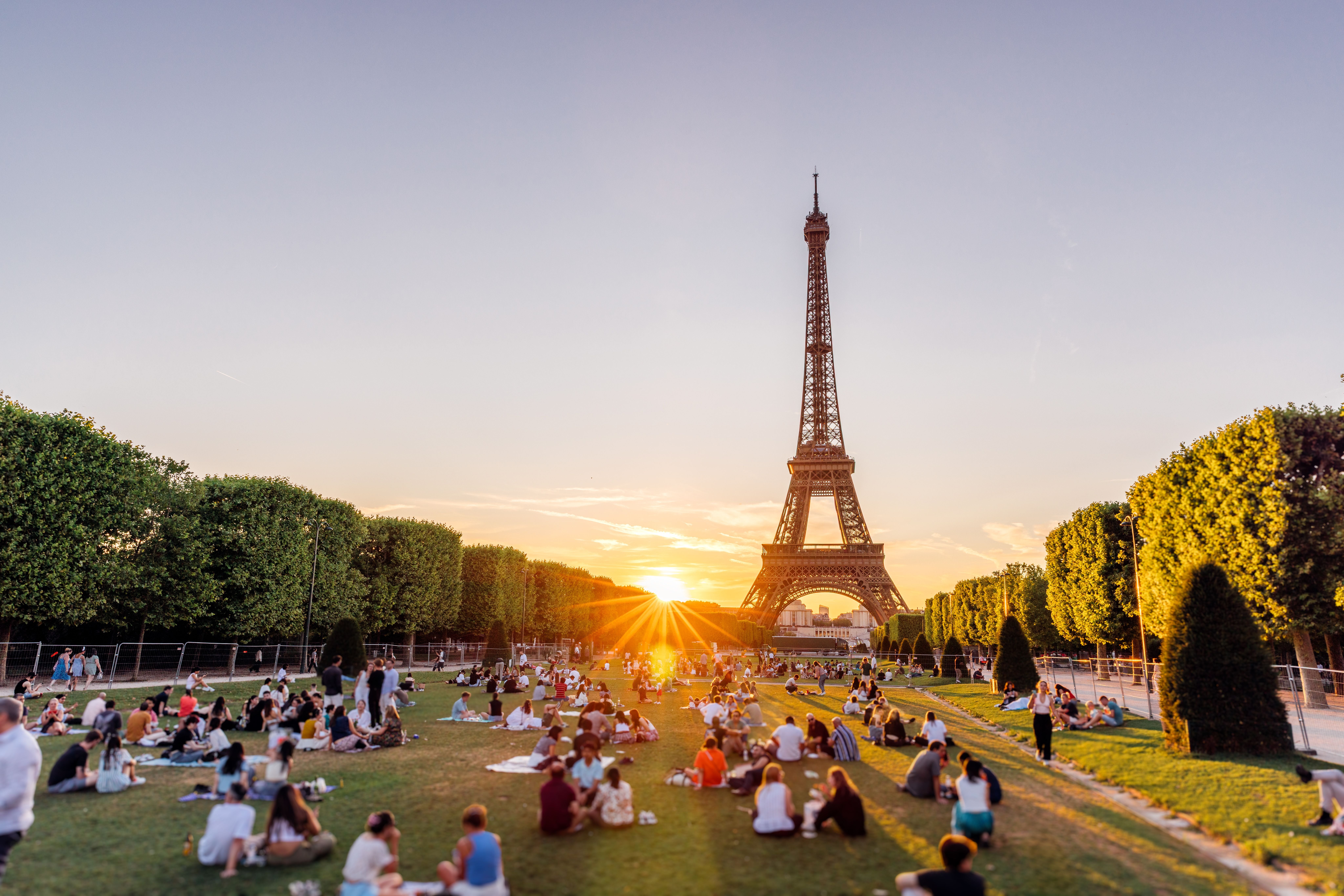 Viele Menschen picknicken im Park vor dem Eiffelturm bei Sonnenuntergang in Paris.