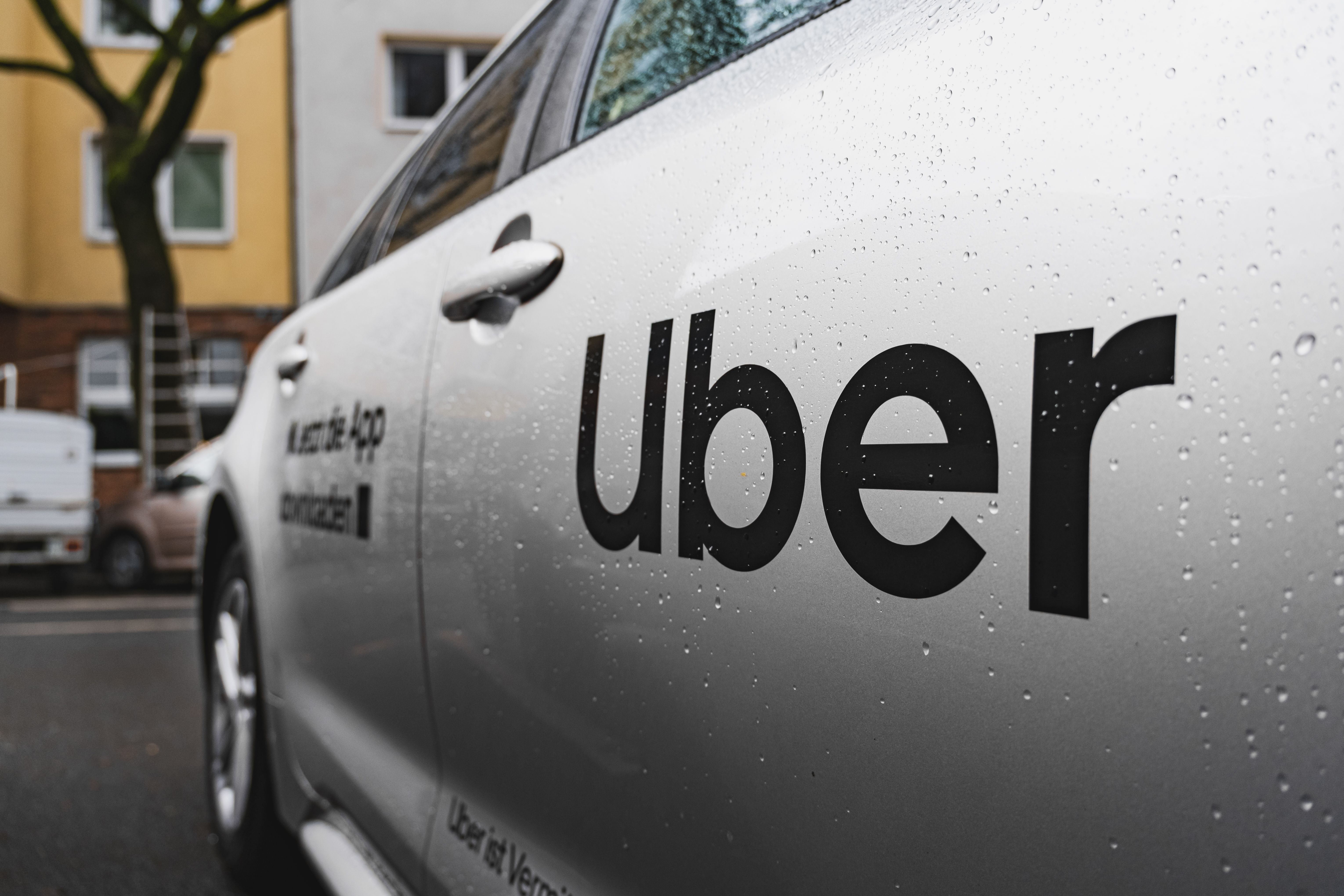 Silbernes Auto mit großem schwarzen Uber-Logo auf der Tür, Wassertropfen auf der Oberfläche.