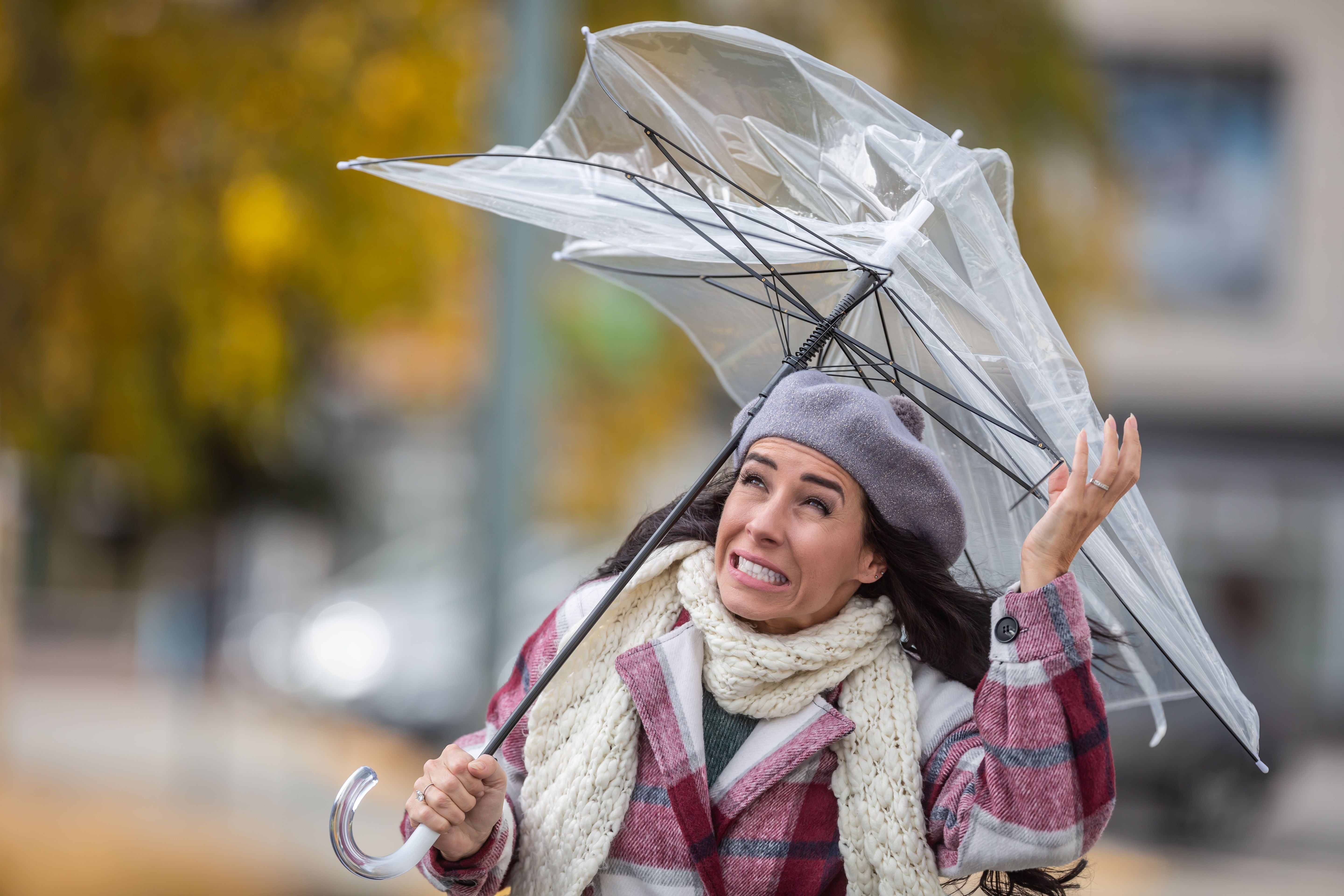 Frau schaut erschrocken auf ihren vom Wind umgestülpten Regenschirm im Herbstwetter.