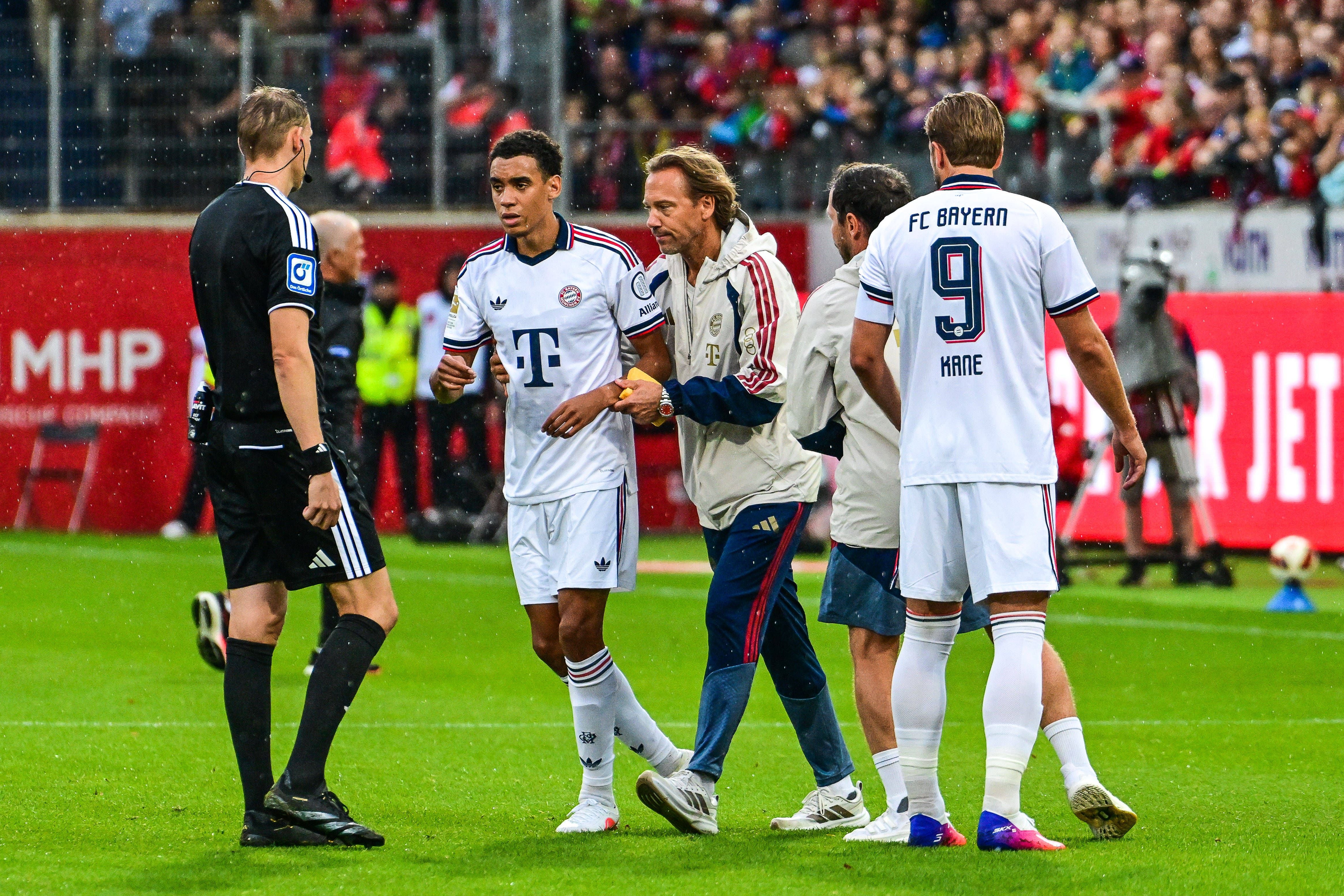Jamal Musiala wird nach einem Zusammenbruch von Ärzten und Betreuern vom Spielfeld begleitet.