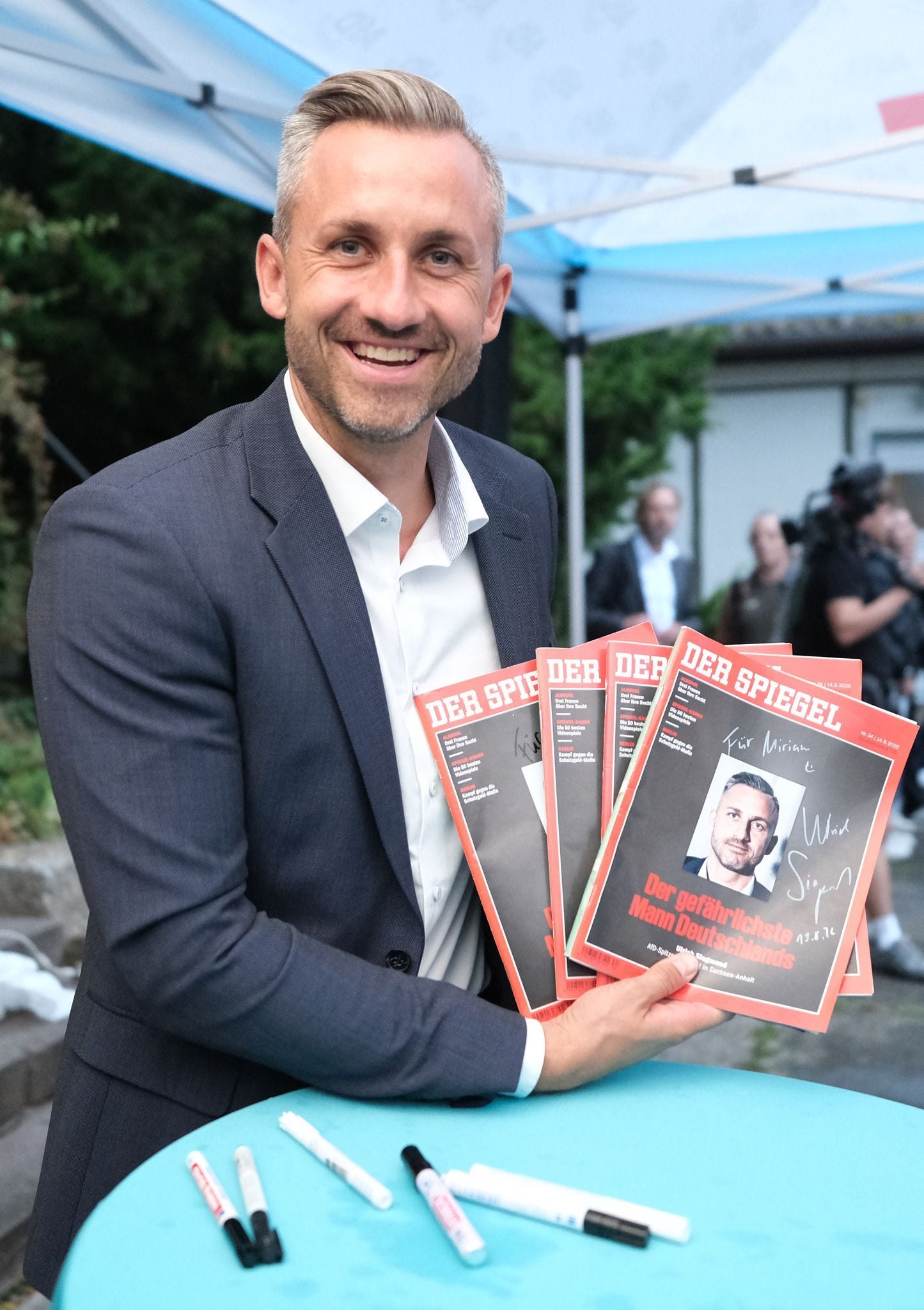 Ein Mann im Anzug hält mehrere Ausgaben des Magazins "Der Spiegel" mit seinem Porträt am Titel.