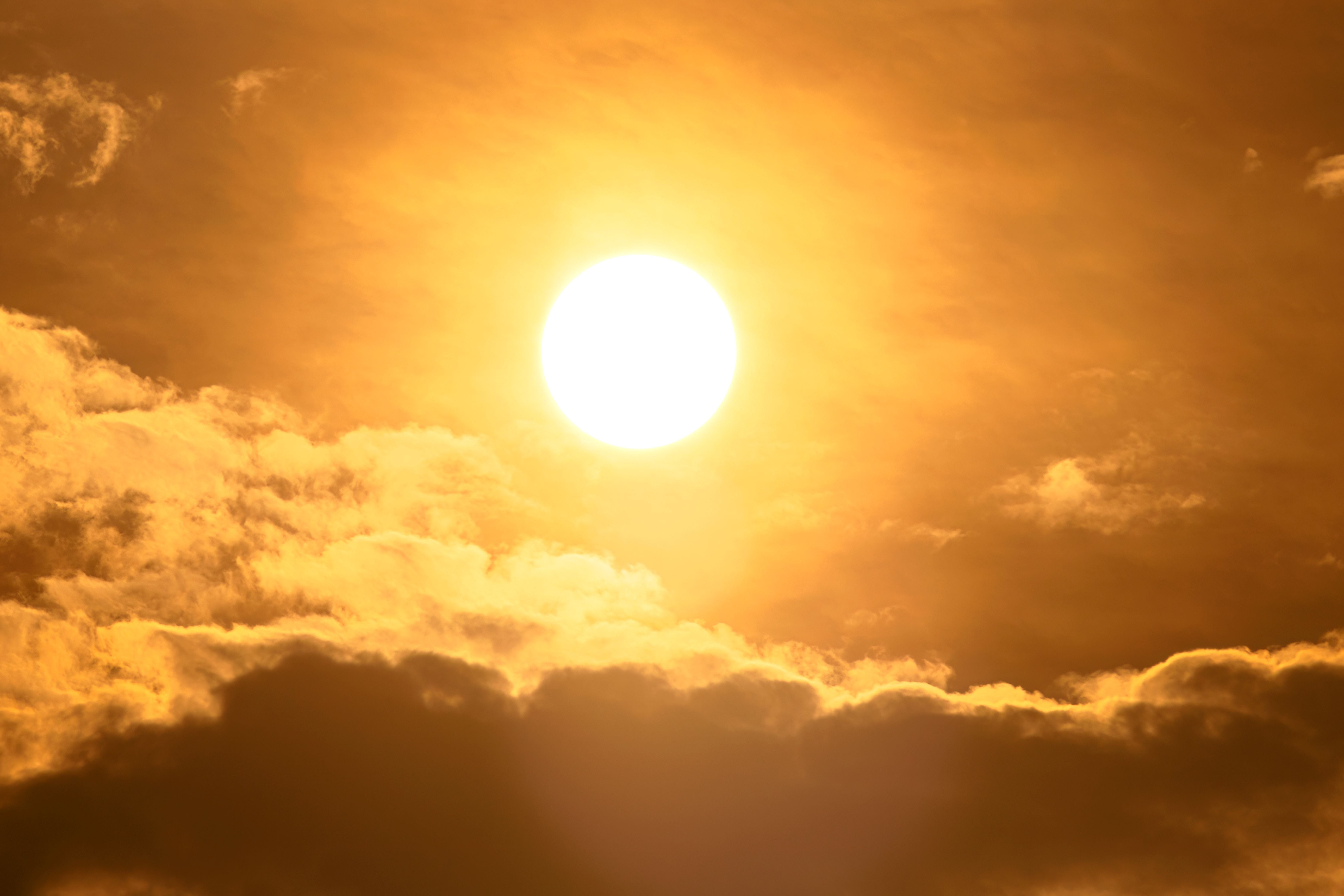 Die Sonne scheint grell durch gelb-orangene Wolken, die Hitze und Trockenheit symbolisieren.