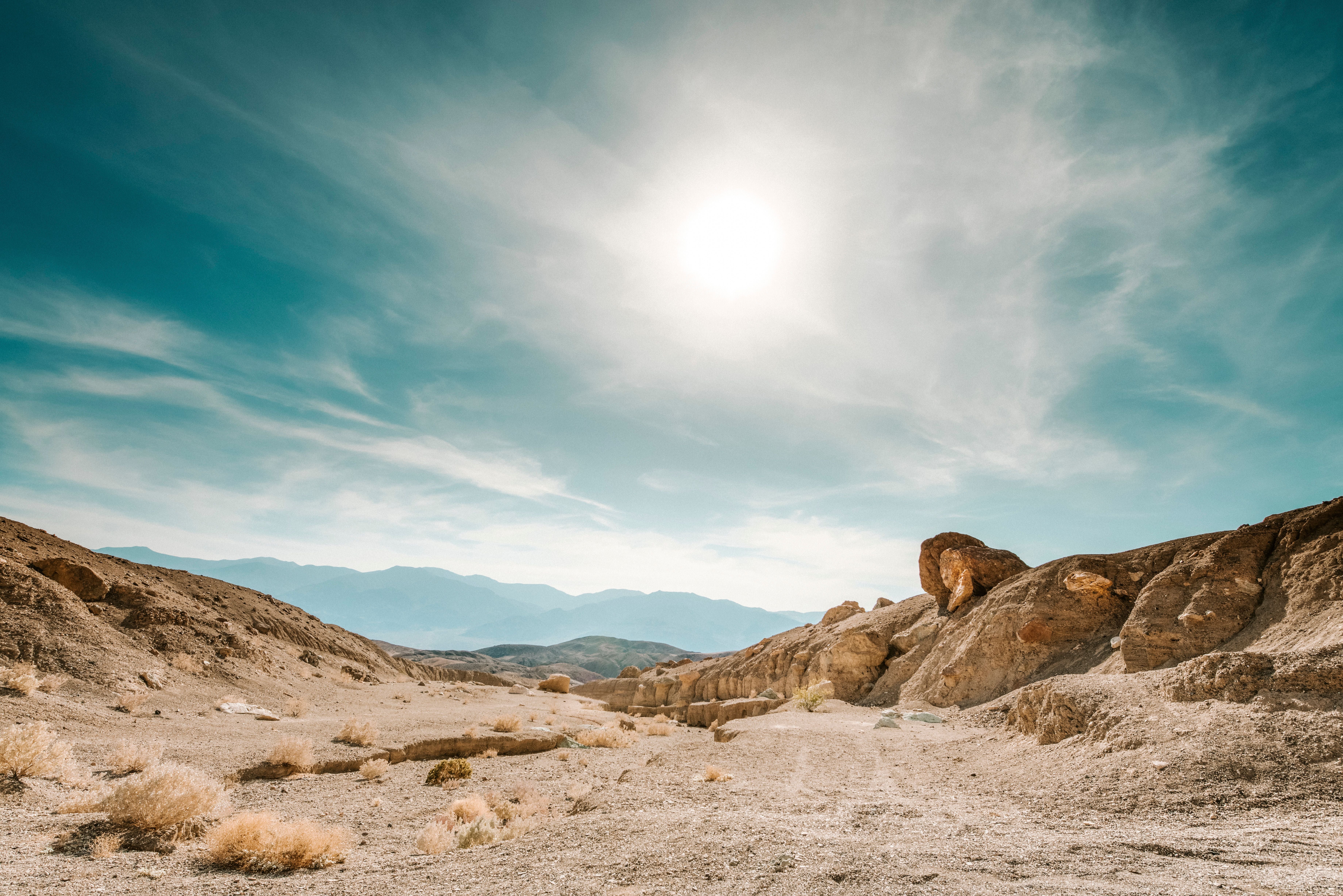 Sonnige Wüstenlandschaft im Death Valley mit Felsen, Staub und trockenen Büschen unter blauem Himmel.
