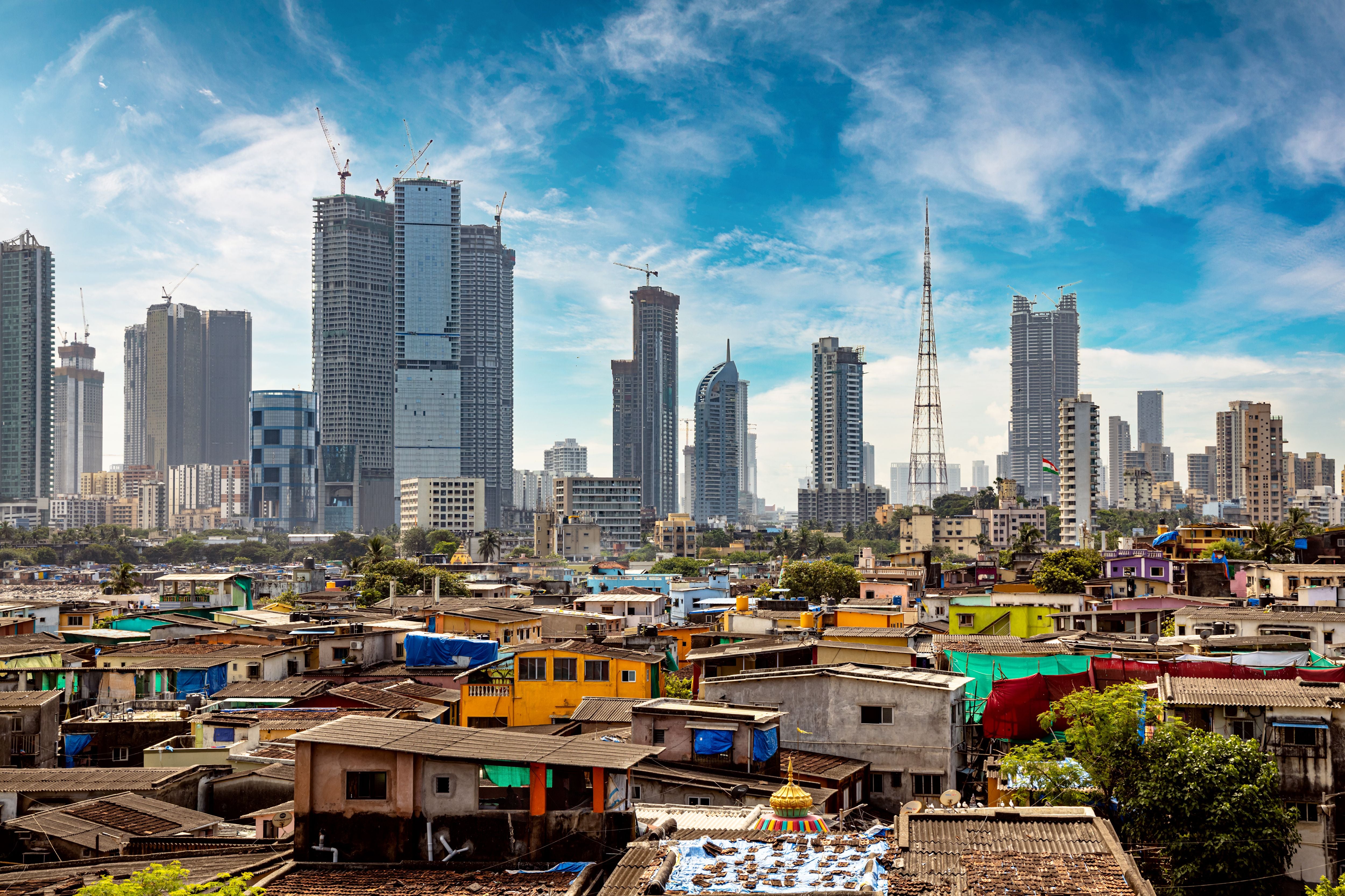 Slums von Mumbai mit bunten Dächern vor modernen Wolkenkratzern und Baustellen im Hintergrund.