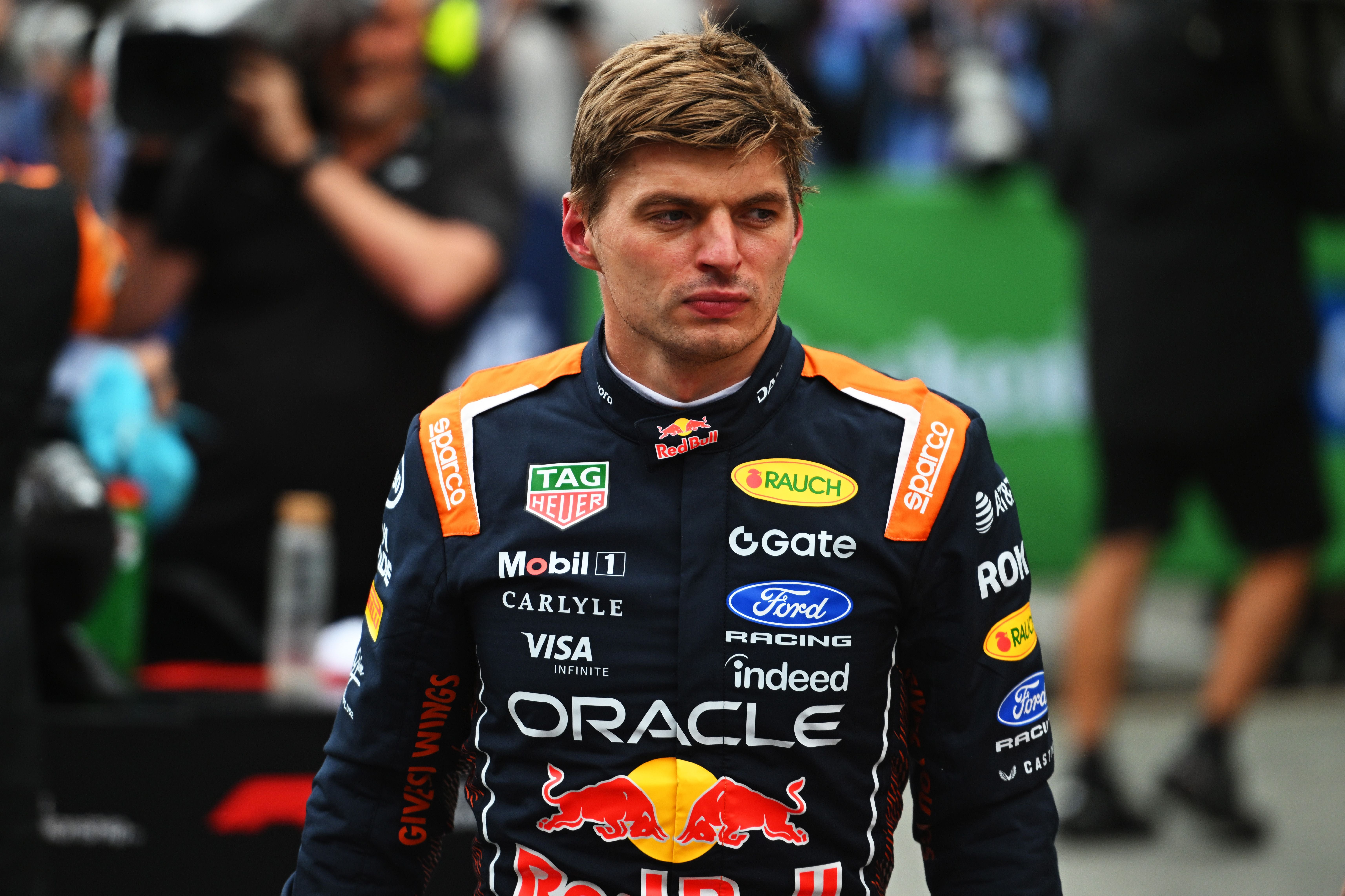 Ein Rennfahrer im Red-Bull-Rennanzug steht fokussiert im Fahrerlager einer Formel-1-Strecke.