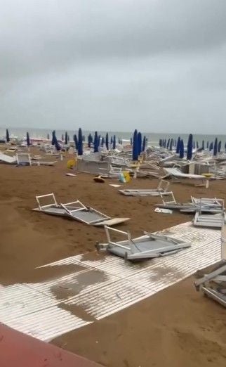 Viele umgestürzte Liegen und geschlossene Sonnenschirme an einem stürmischen Strand in Lignano.