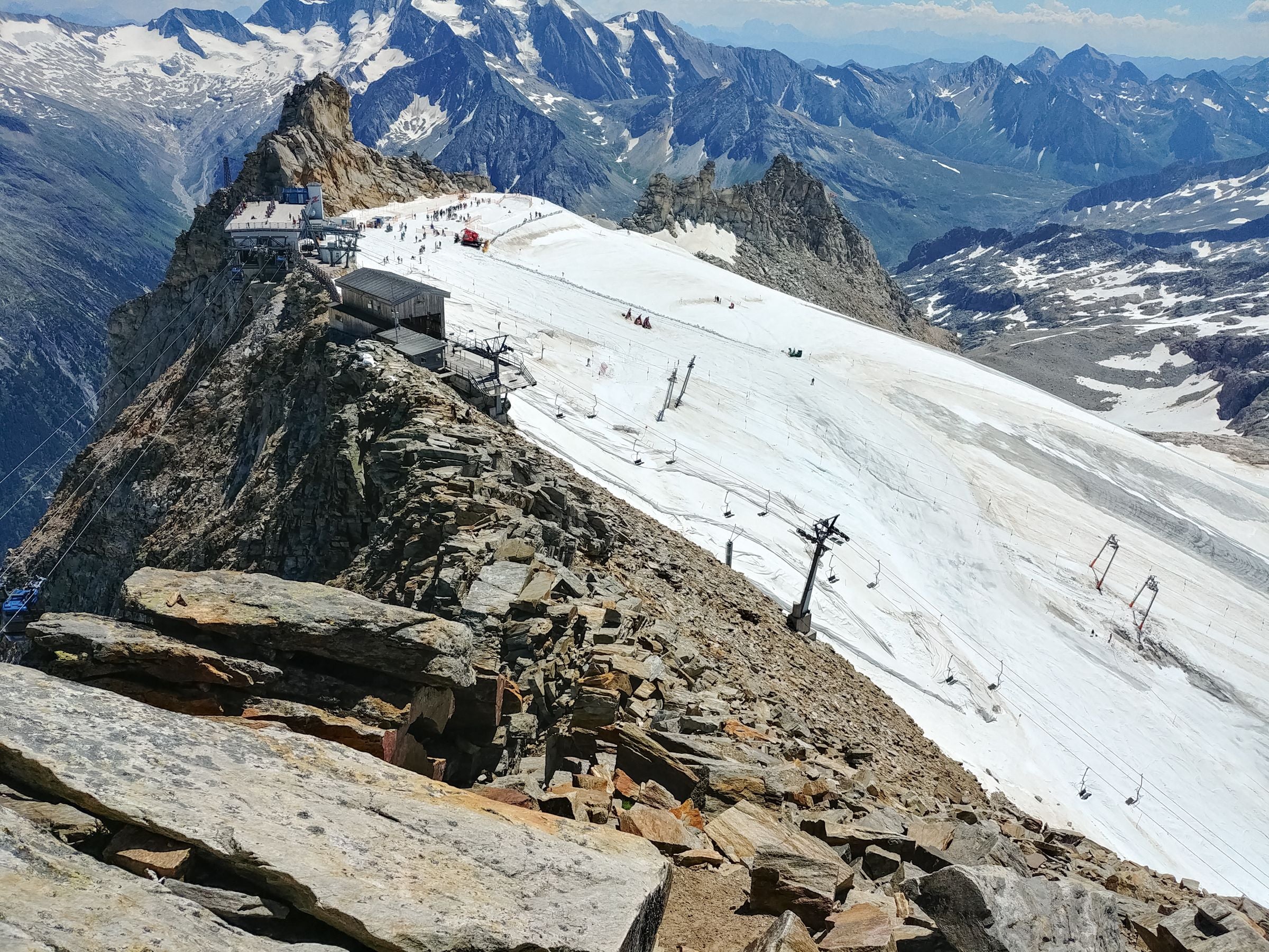 Bergstation mit Gletscher und Skiliften in den Alpen, umgeben von schneebedeckten Bergen.