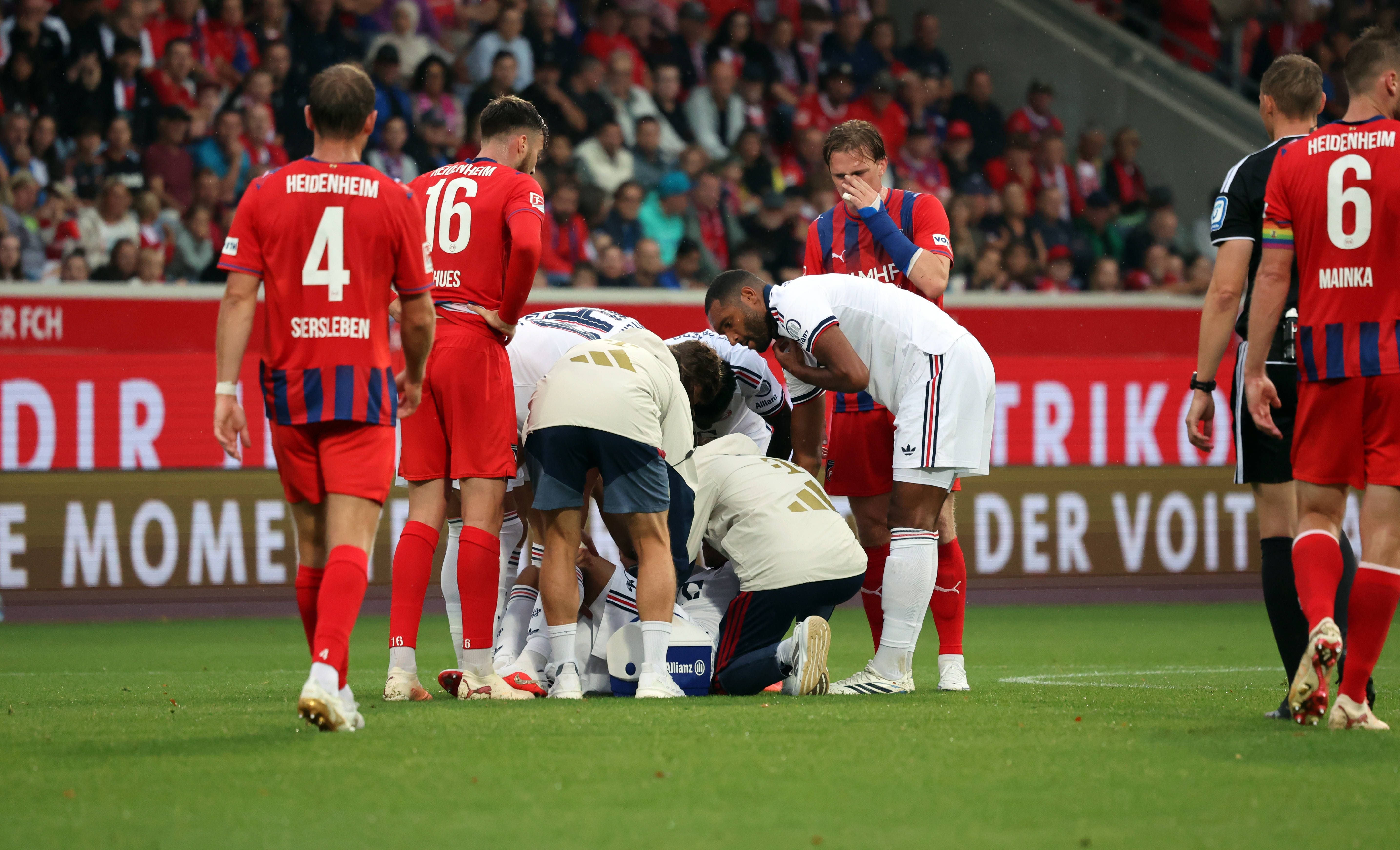 Spieler und Betreuer kümmern sich am Boden um einen verletzten Bayern-Spieler beim Fußballspiel.