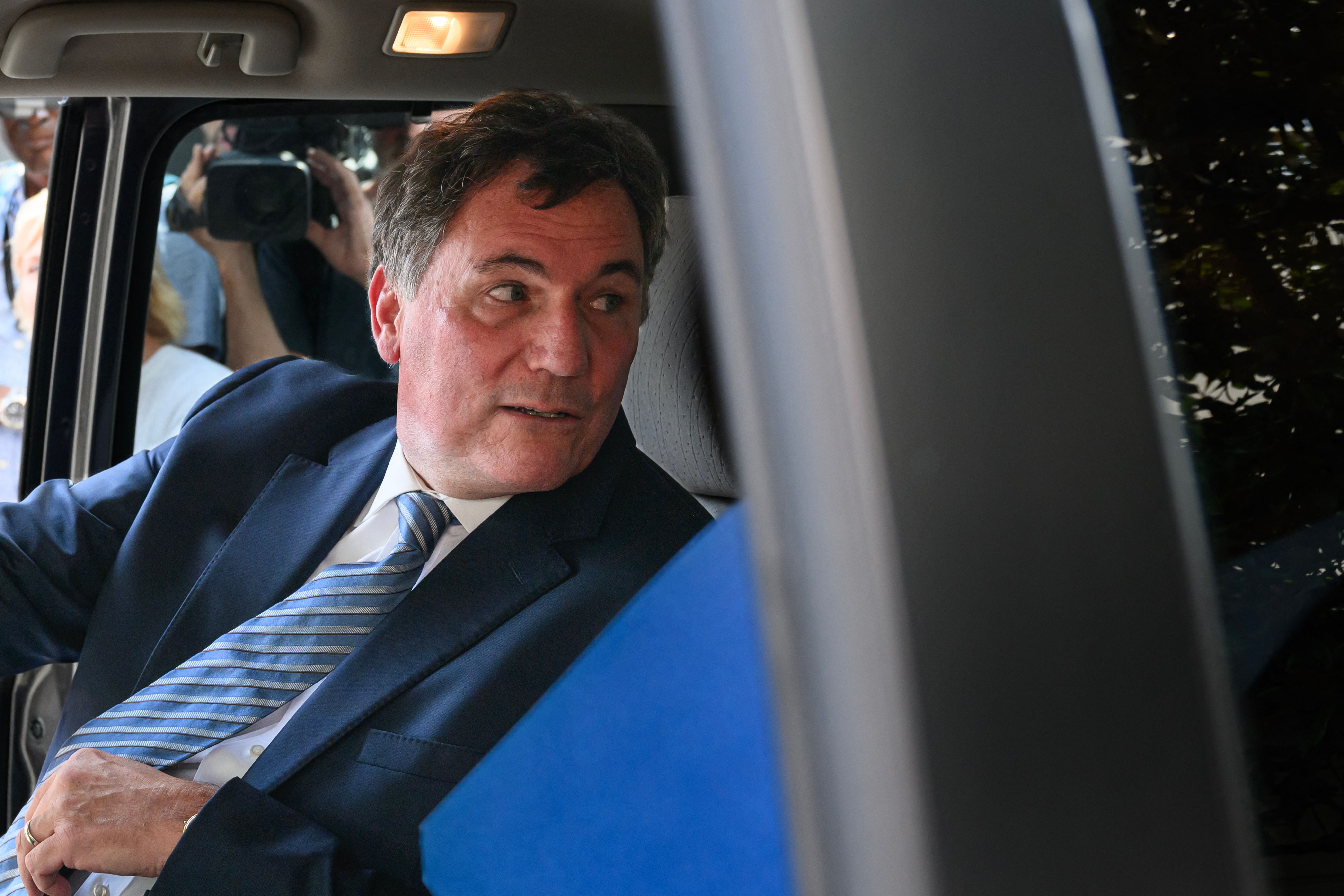 Ein Mann im Anzug sitzt in einem Auto und schaut aus dem Fenster nach draußen.