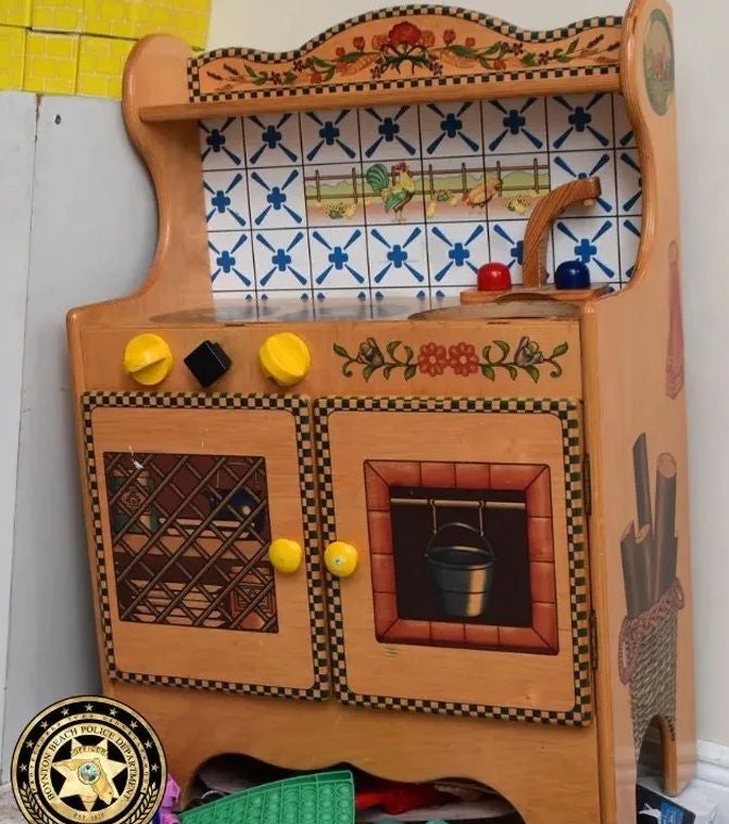 Holzspielzeugherd mit bemalten Blumen, Kacheln und zwei Türen, daneben Polizeiemblem.