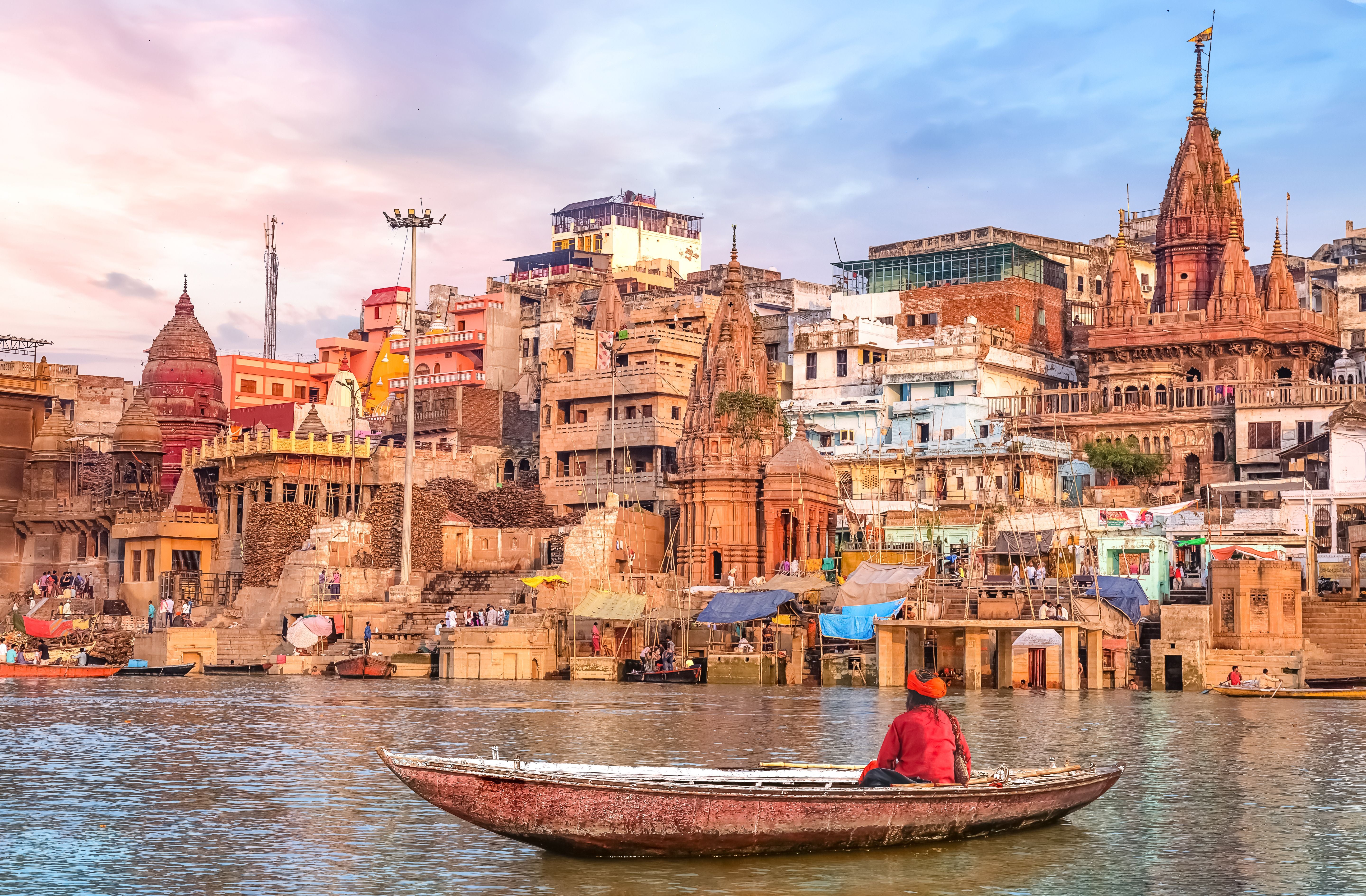 Ein Sadhu sitzt in einem Boot auf dem Ganges vor den Tempeln und Gebäuden von Varanasi bei Sonnenuntergang.
