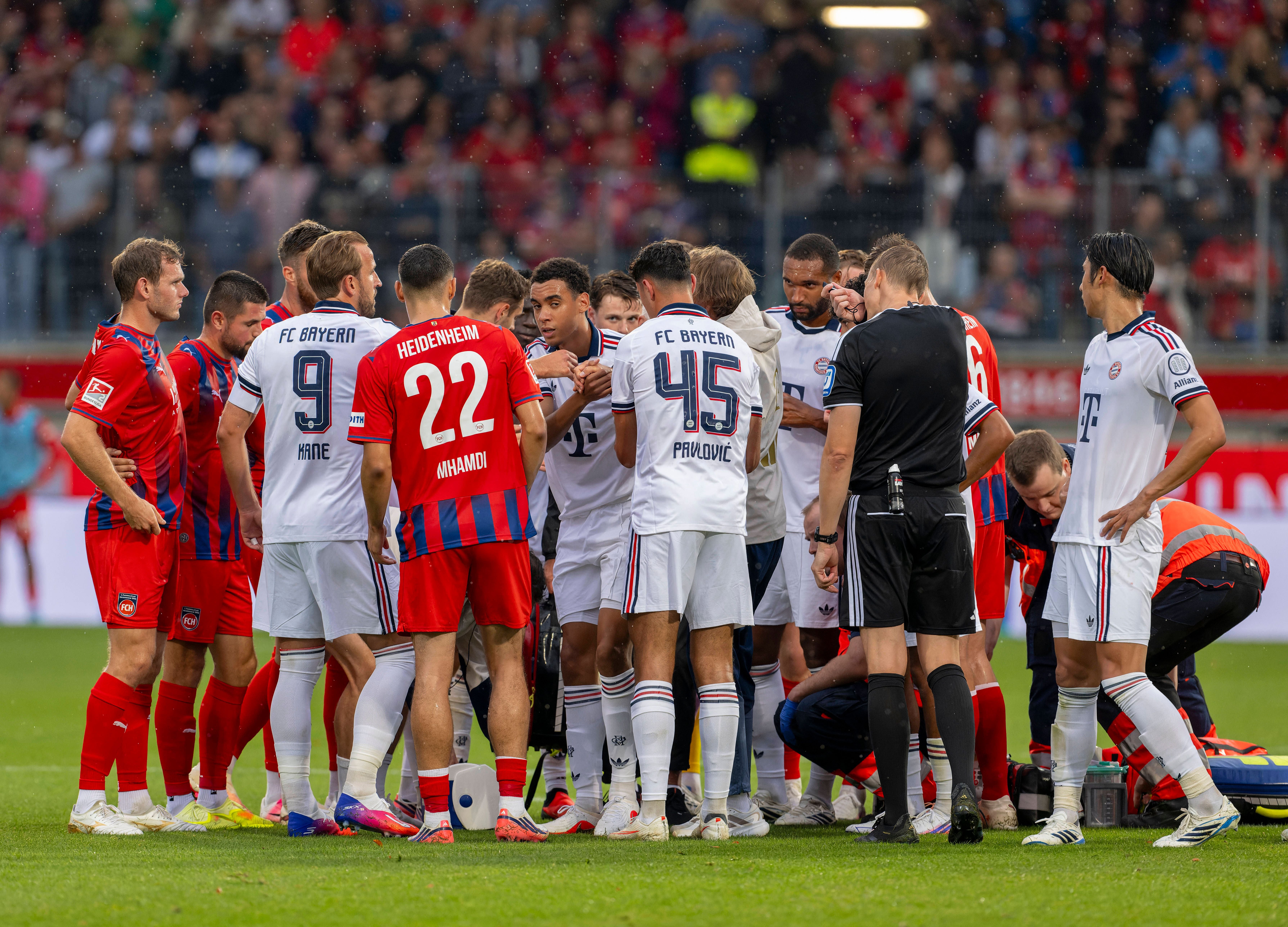 Spieler beider Teams stehen besorgt um Jamal Musiala, der am Boden medizinisch versorgt wird.