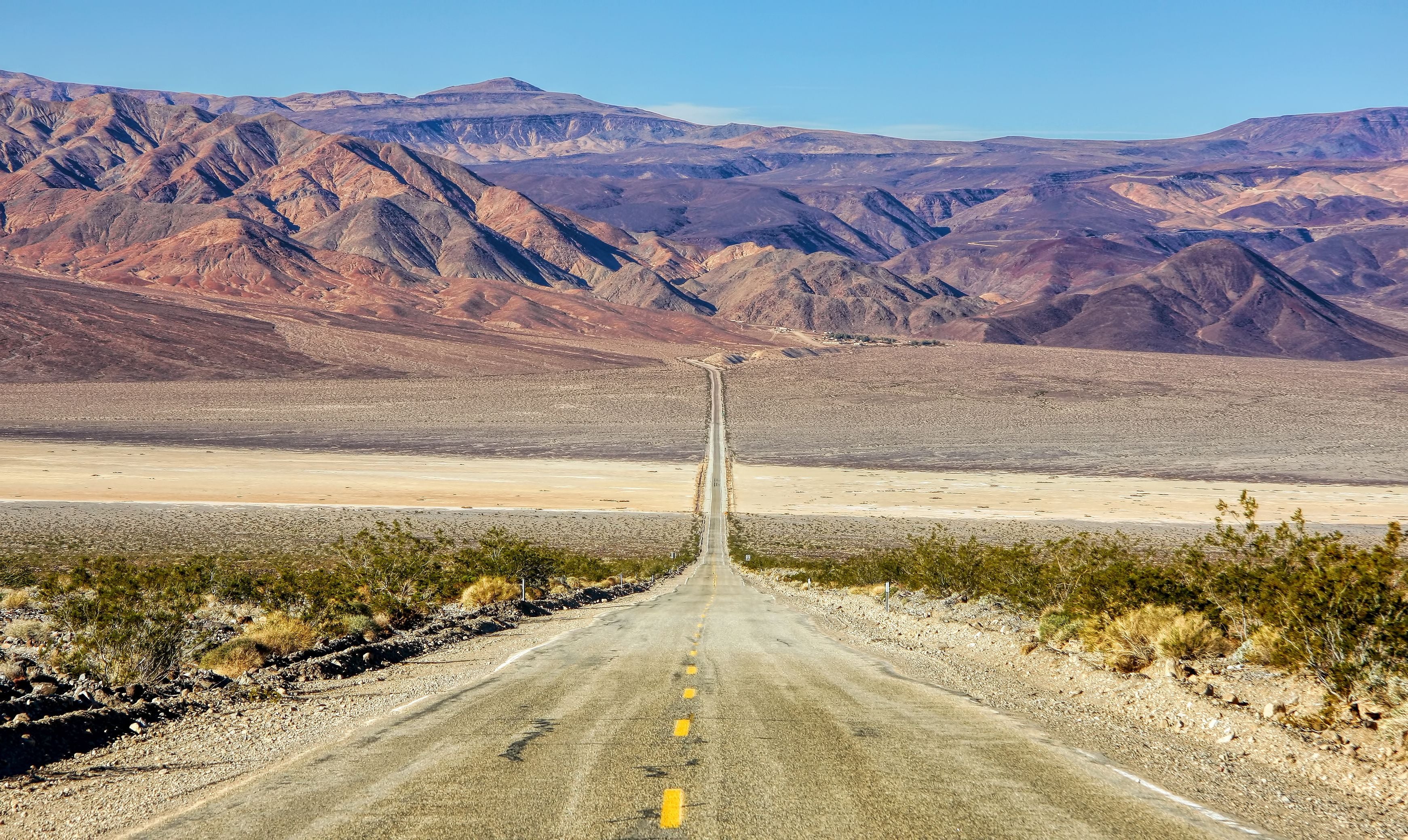 Gerade Straße führt durch trockene Wüste auf Berge im Death Valley, Kalifornien, zu.