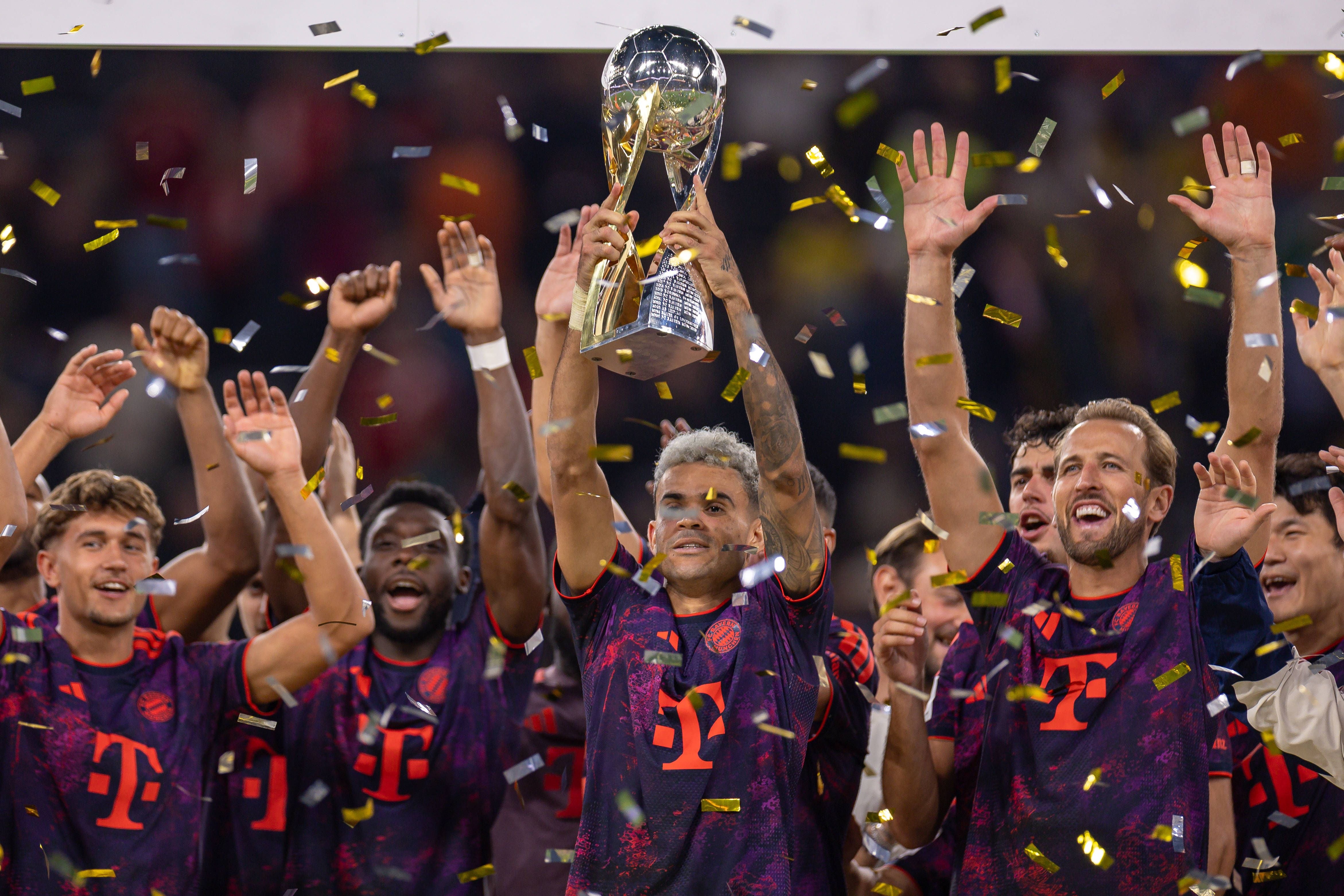 Spieler des FC Bayern München jubeln mit dem Supercup-Pokal, umgeben von goldenen Konfetti.