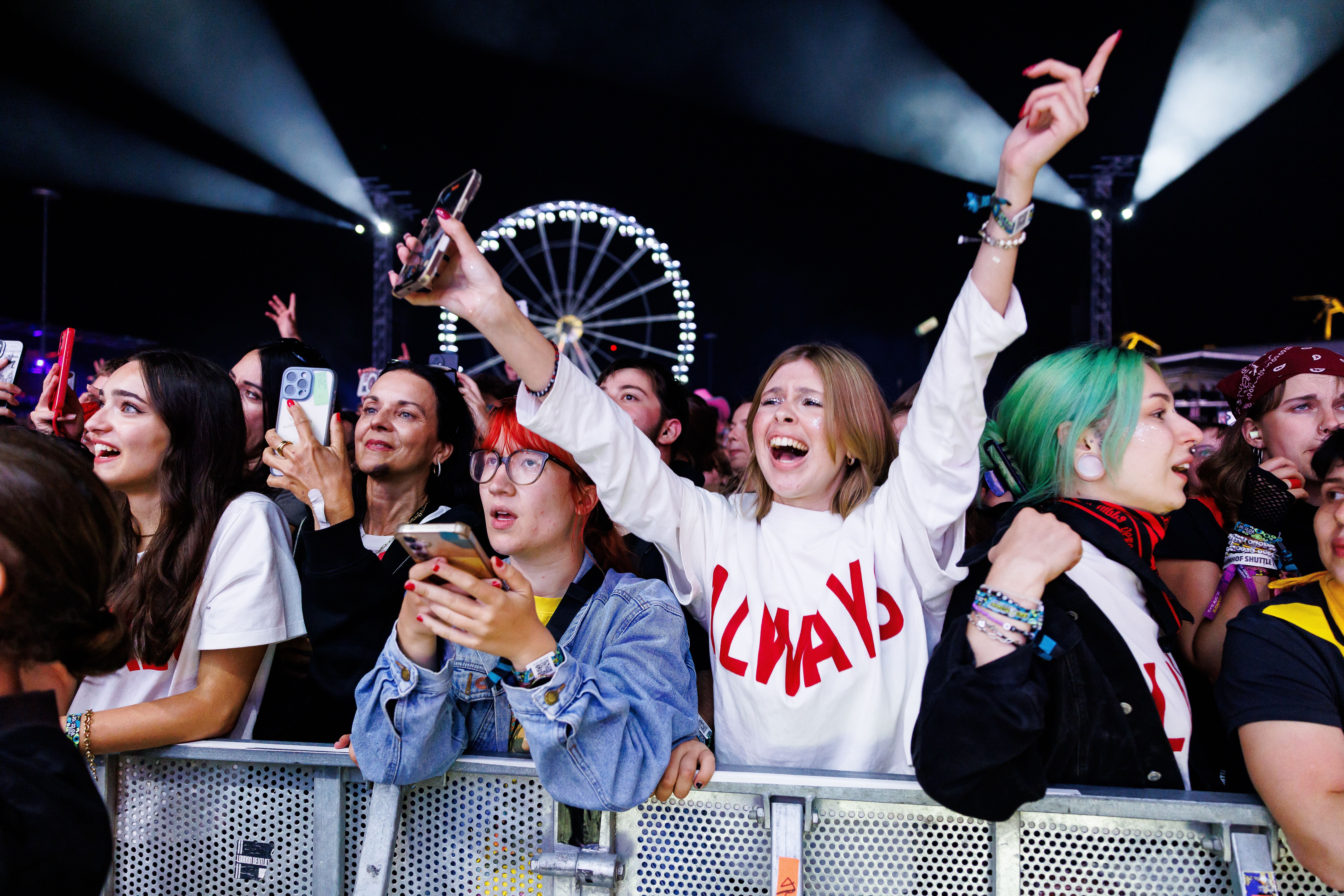 Jubelnde Konzertbesucher vor der Bühne bei einem Open-Air-Festival, im Hintergrund ein Riesenrad.