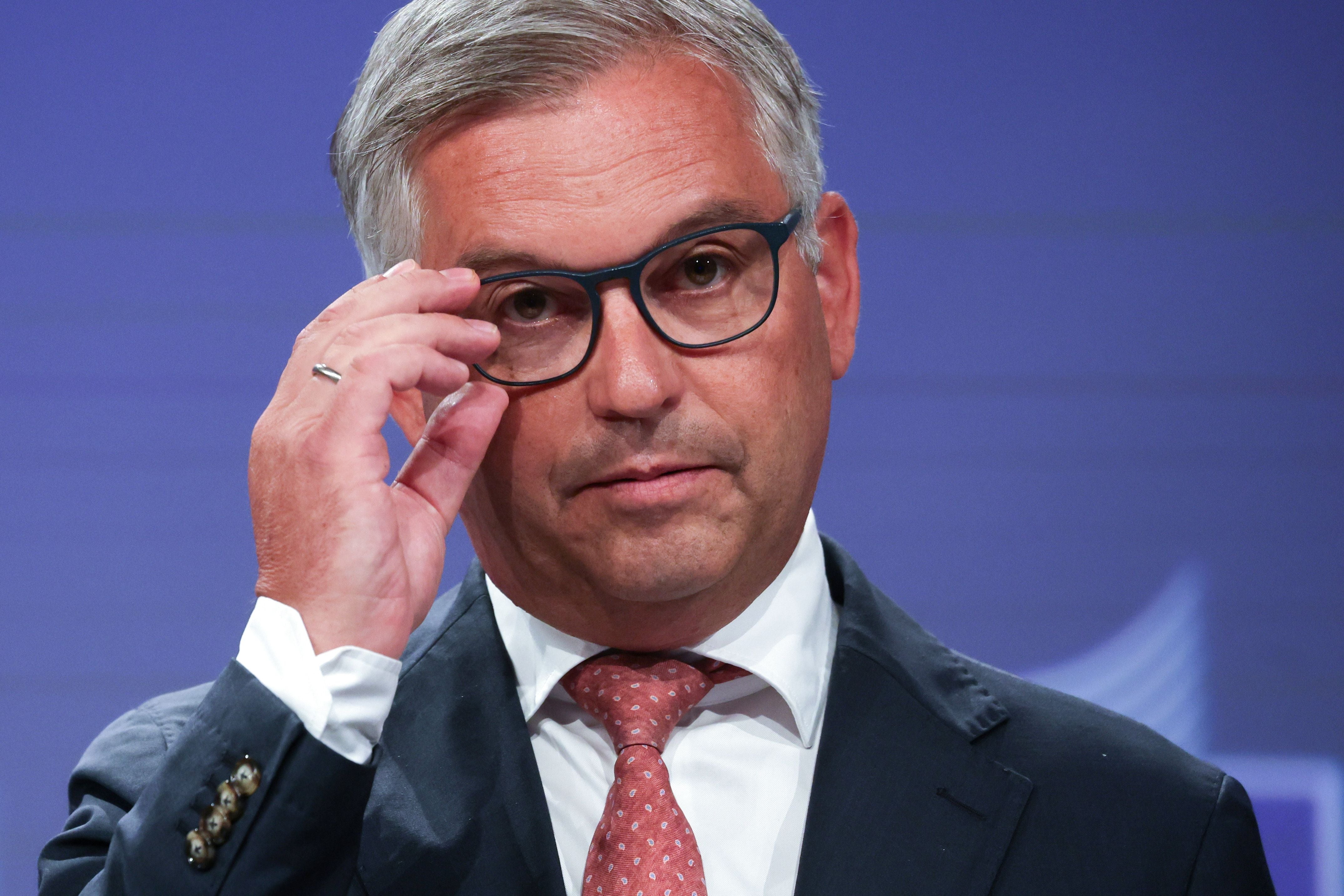 Ein Mann im Anzug und mit Brille spricht auf einer Pressekonferenz vor blauem Hintergrund.