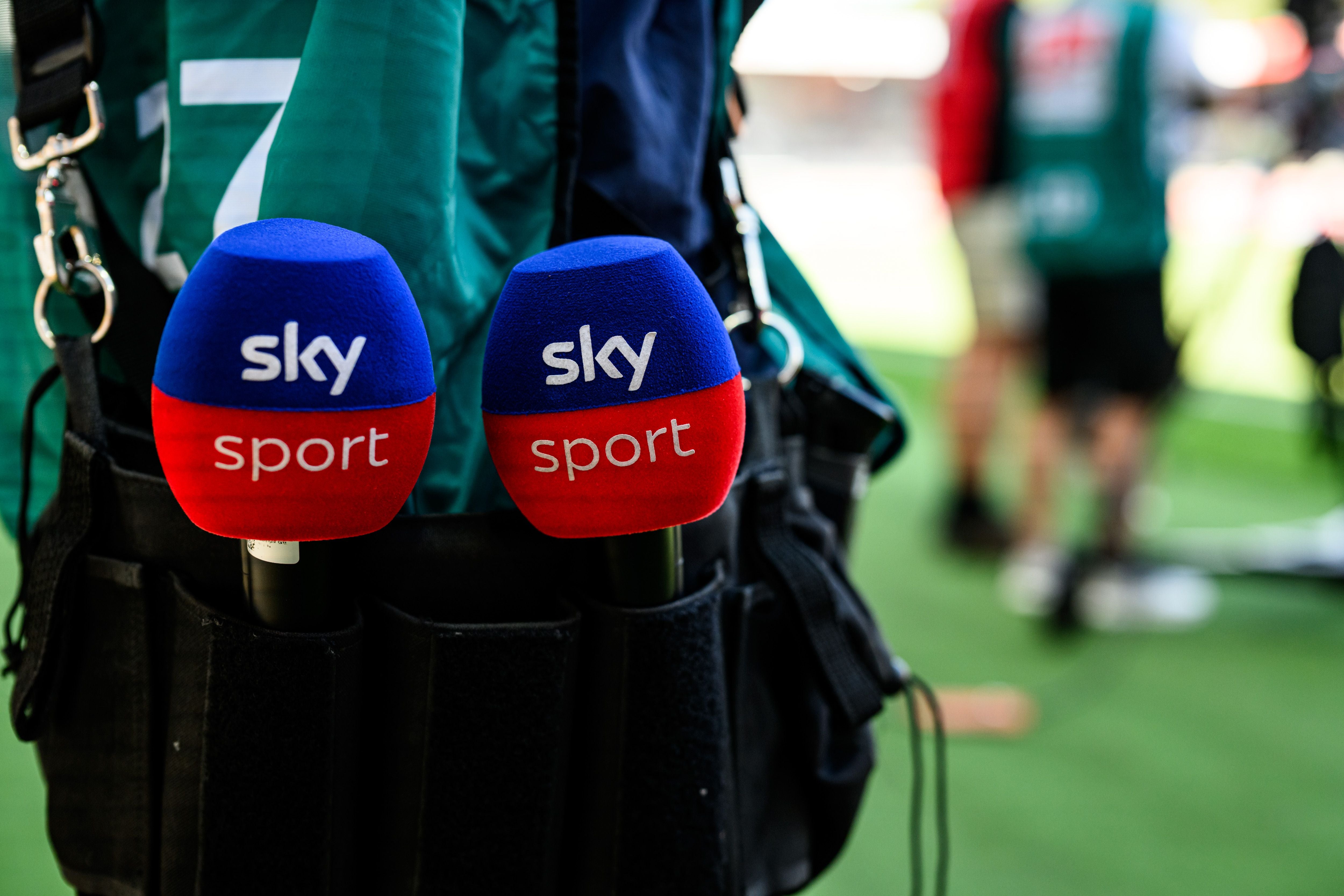 Zwei Mikrofone mit Sky Sport Logo stecken in einer Tasche, unscharfer Hintergrund im Stadion.