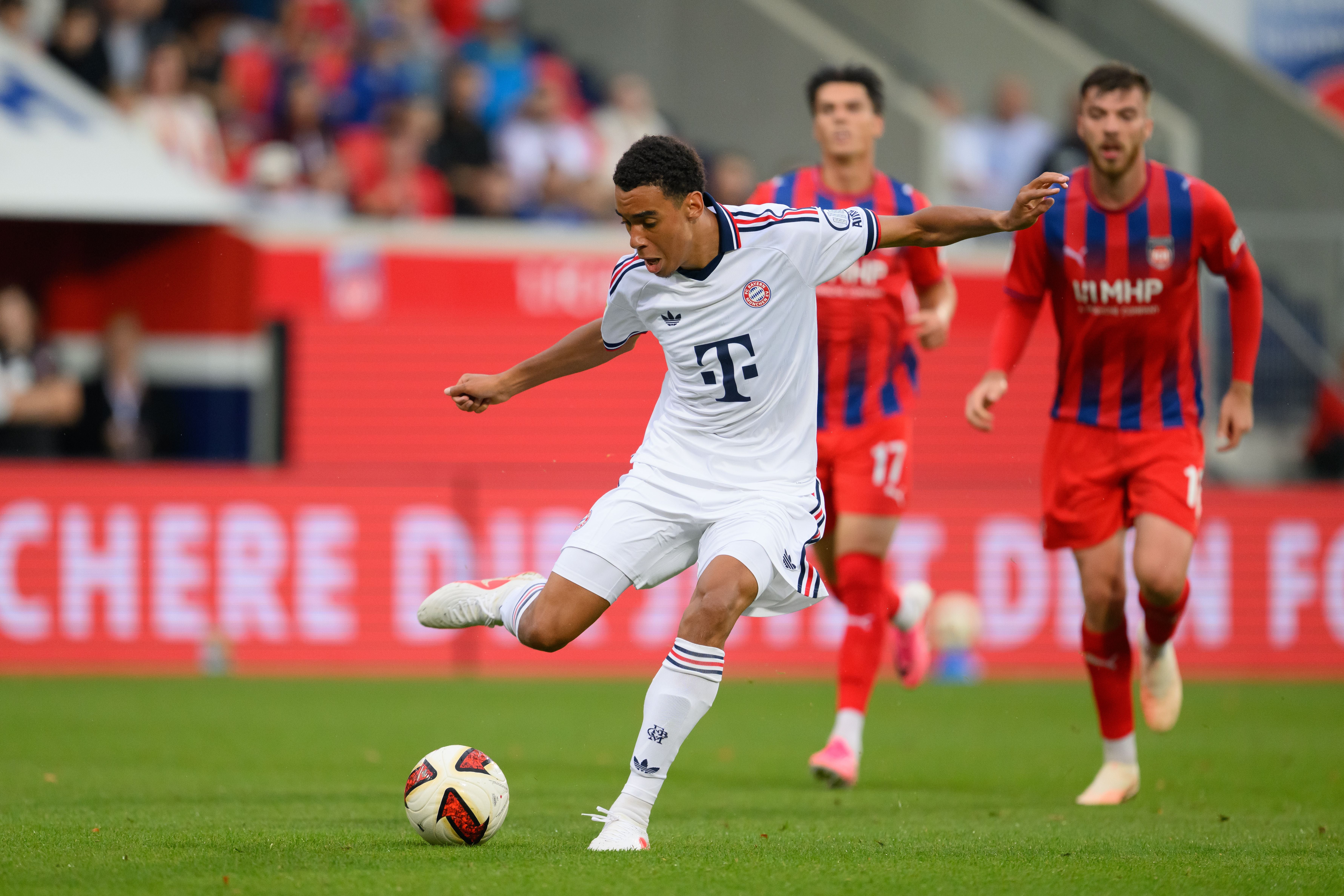 Ein Fußballspieler von Bayern München schießt den Ball, zwei Gegner verfolgen ihn im Hintergrund.