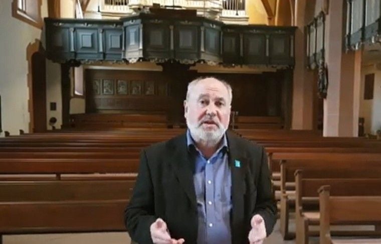 Ein älterer Mann steht in einer leeren Kirche vor leeren Holzbänken und einer Orgel.