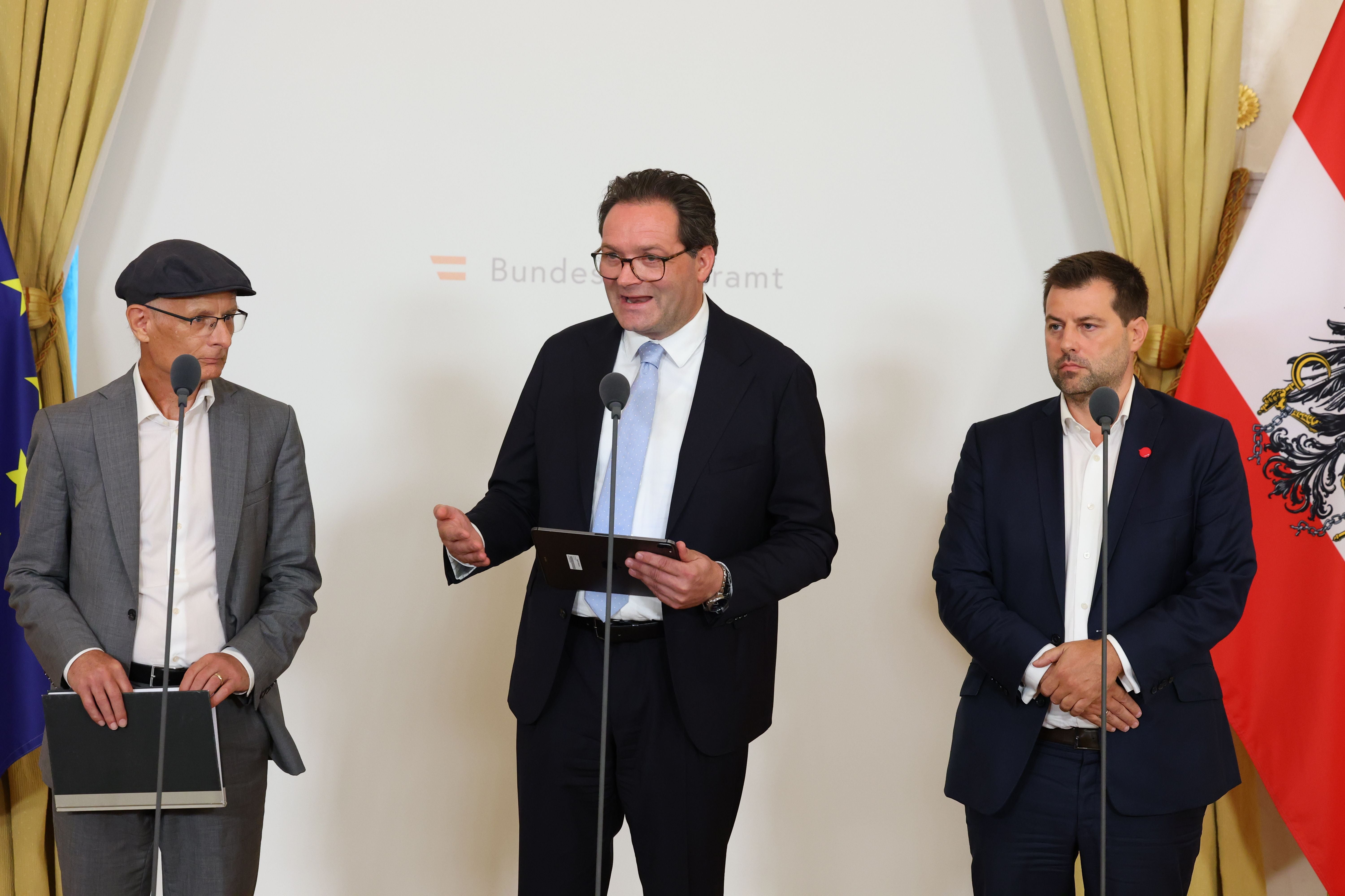 Drei Männer bei einer Pressekonferenz im Bundeskanzleramt mit EU- und Österreich-Flagge im Hintergrund.