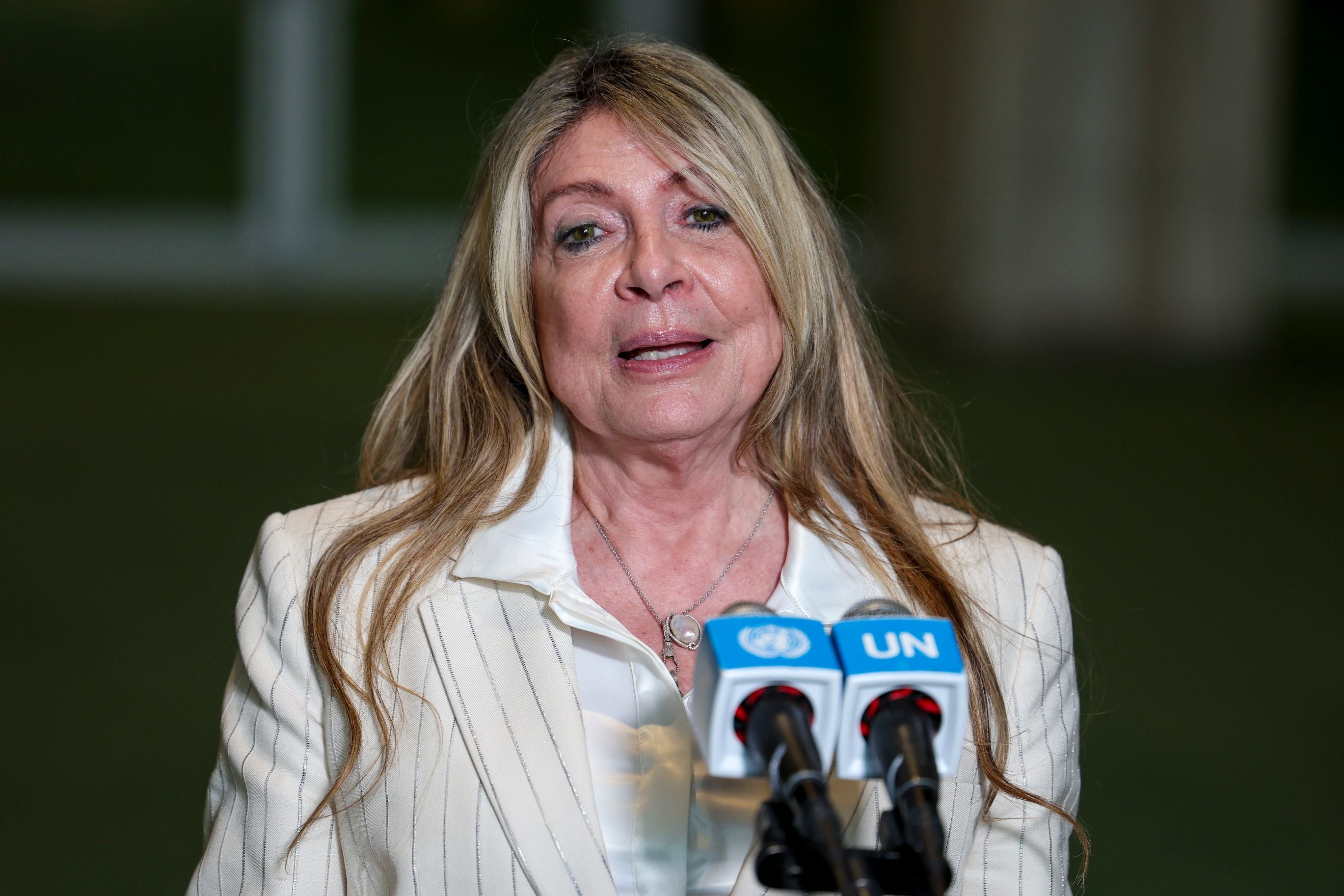Frau spricht bei einer Pressekonferenz vor UN-Mikrofonen in einem hellen Anzug.