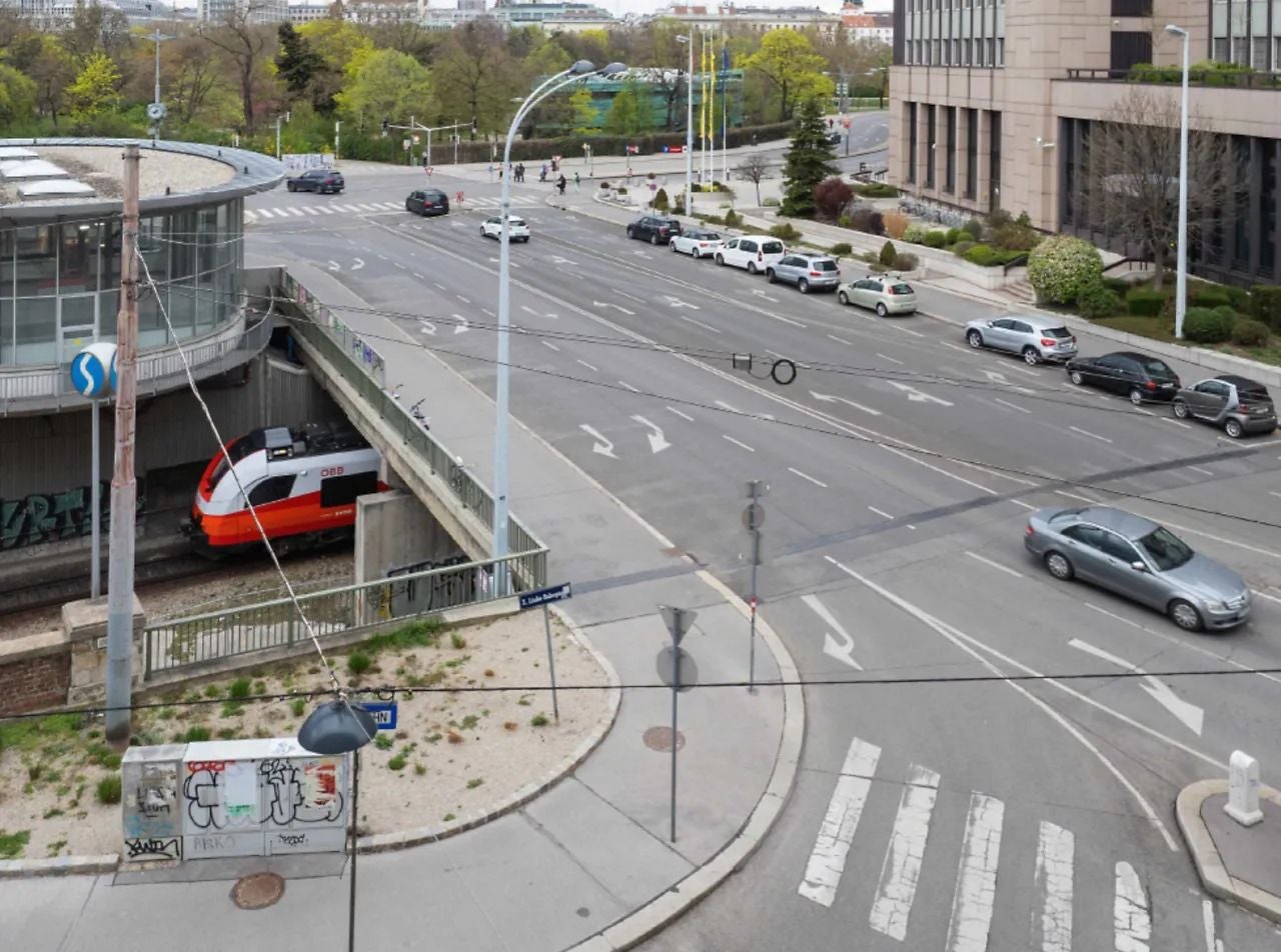 Straßenansicht mit Zebrastreifen, einfahrendem Zug und geparkten Autos an der Großen Ungarbrücke.