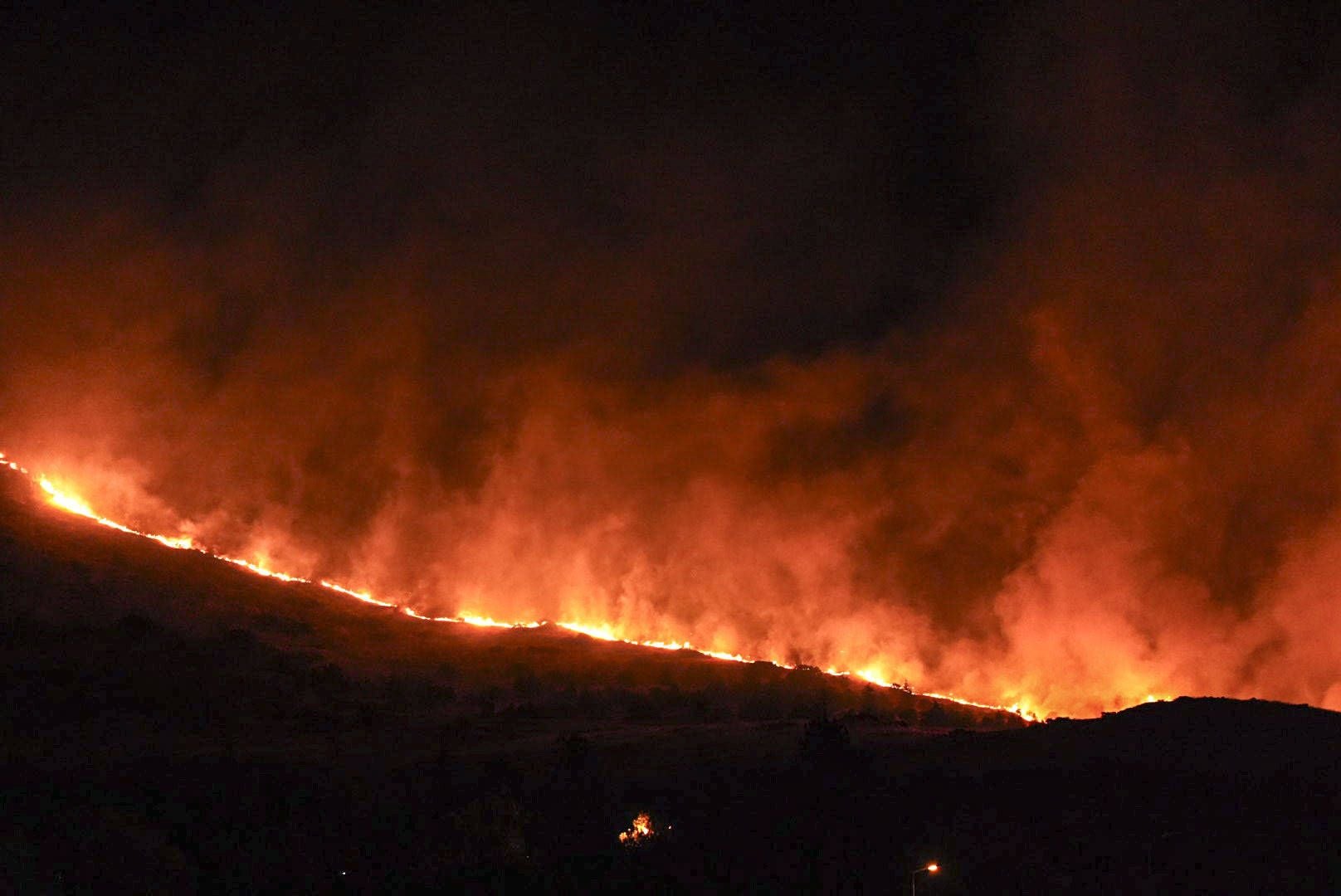 Großes Feuer mit starker Rauchentwicklung in einem bewaldeten Gebiet bei Nacht.