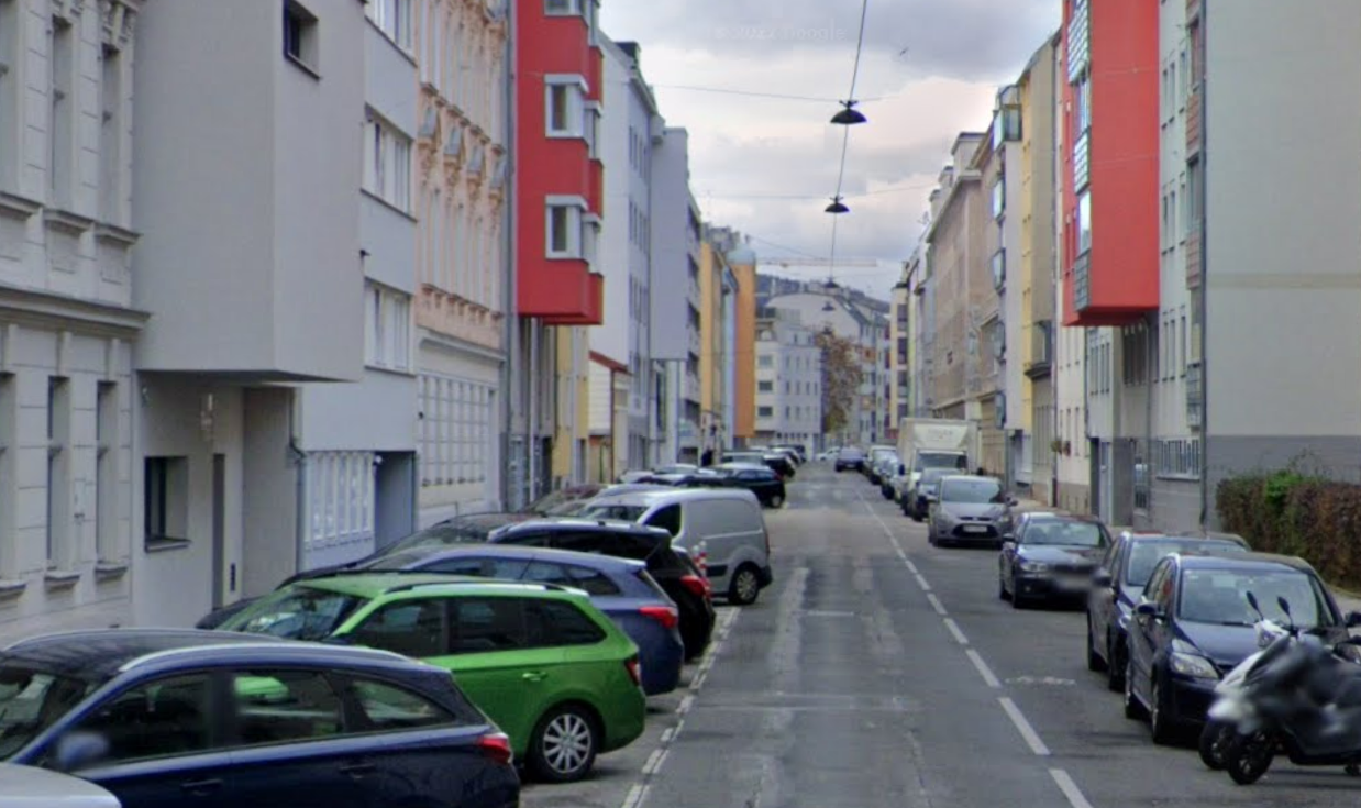 Schmale Wohnstraße in Penzing mit parkenden Autos und mehrstöckigen Häusern links und rechts.