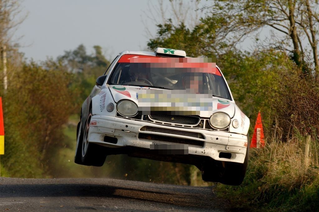 Ein weißer Toyota Corolla WRC springt bei einer Rallye auf einer Landstraße in Irland.
