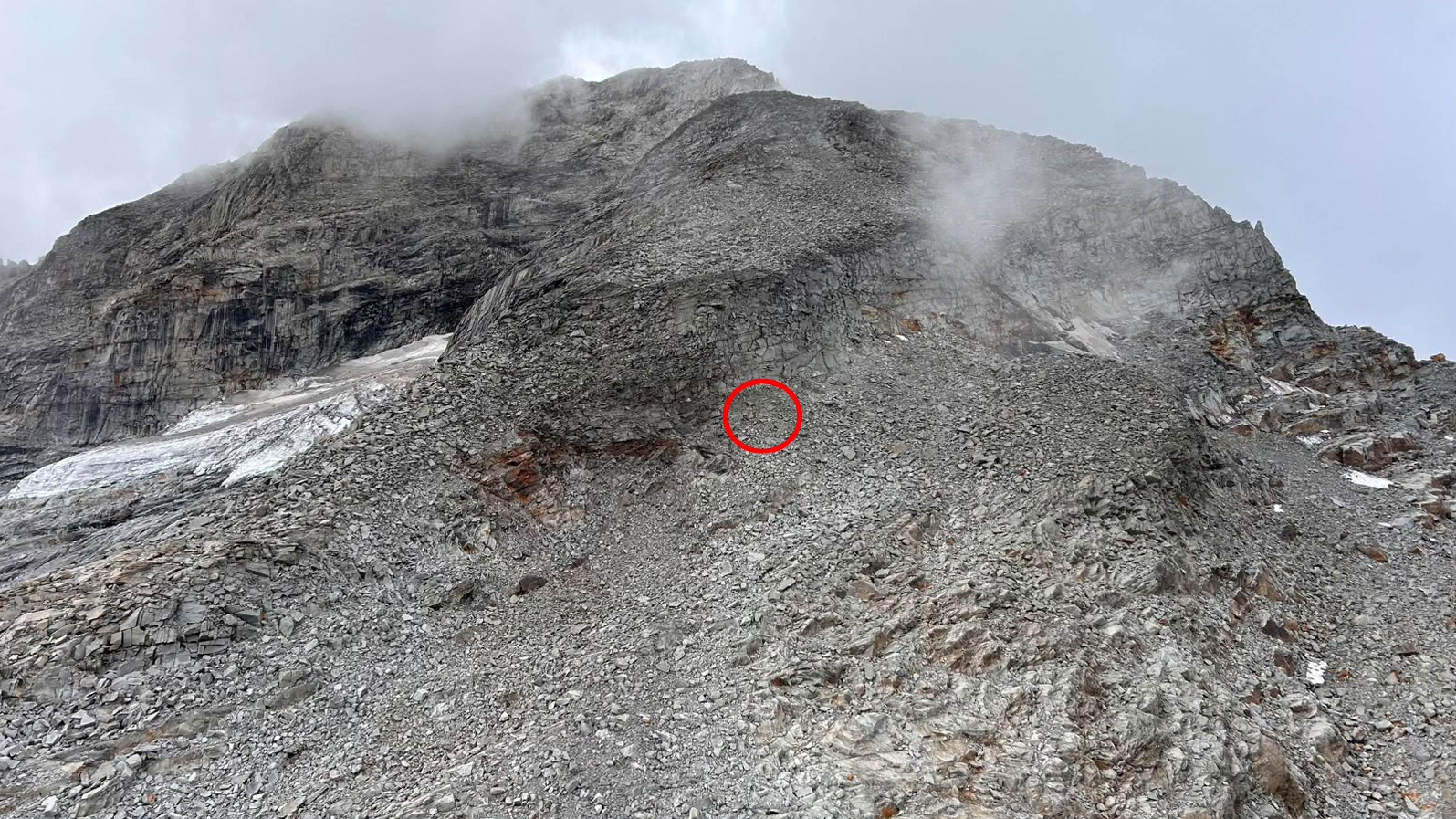 Steiniger Berghang mit Geröll, teils nebelverhangen, roter Kreis markiert eine Stelle.