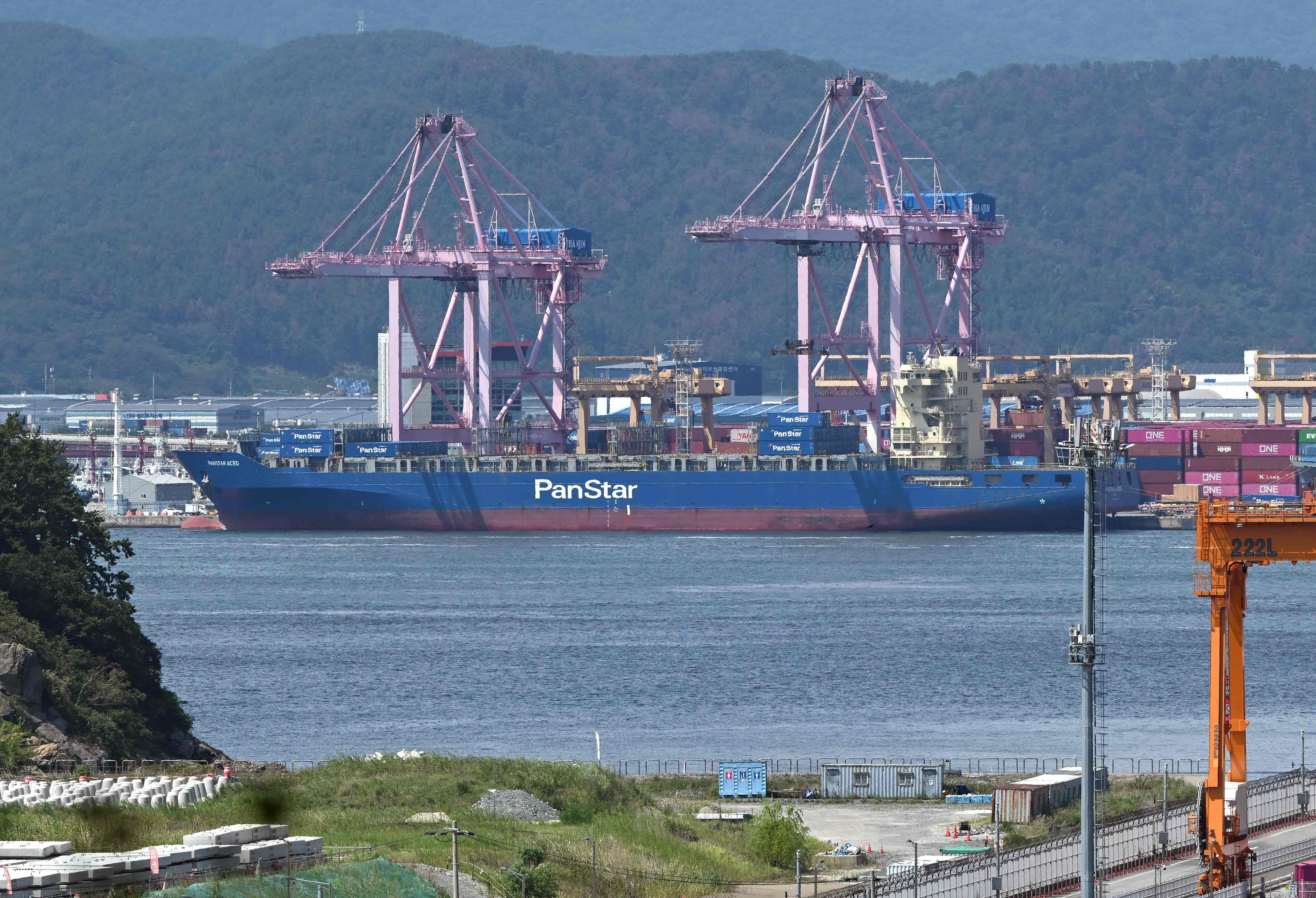 Das Containerschiff PanStar Acro liegt am Hafen von Busan vor Containerkränen vor Anker.