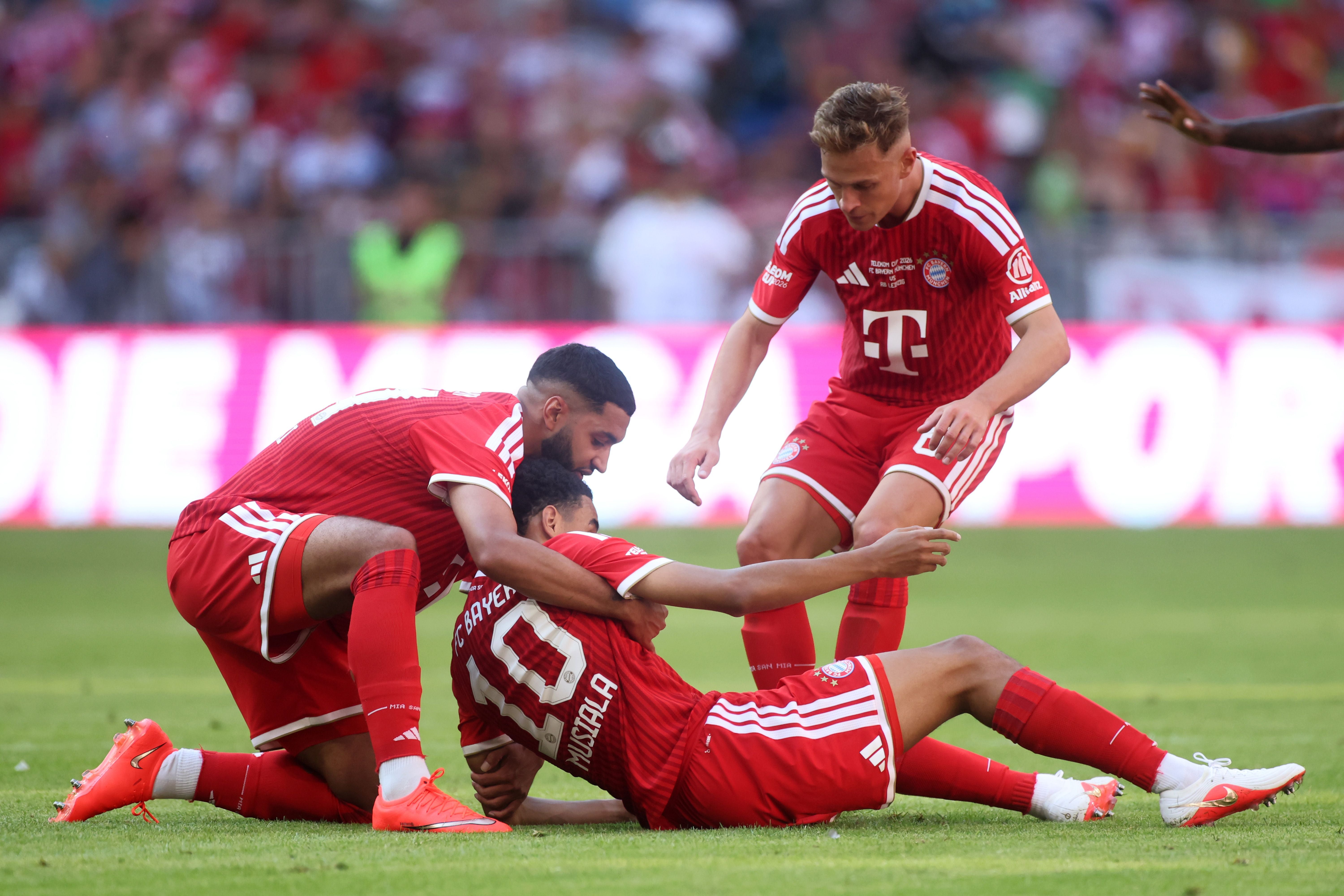 Zwei Bayern-Spieler helfen einem Teamkollegen beim Aufstehen während eines Fußballspiels.