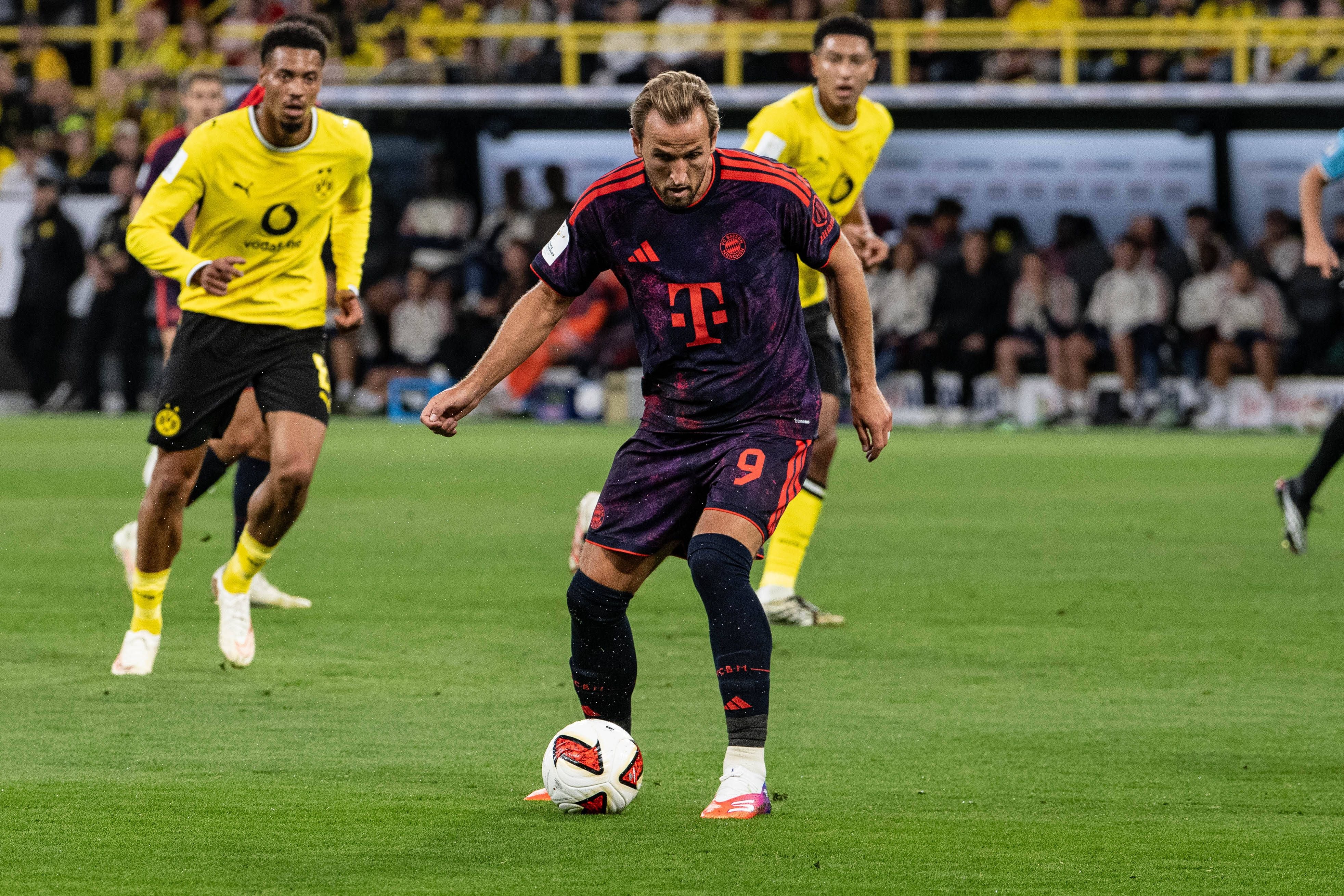 Ein Fußballspieler von Bayern München spielt den Ball, während zwei Dortmunder Spieler zuschauen.