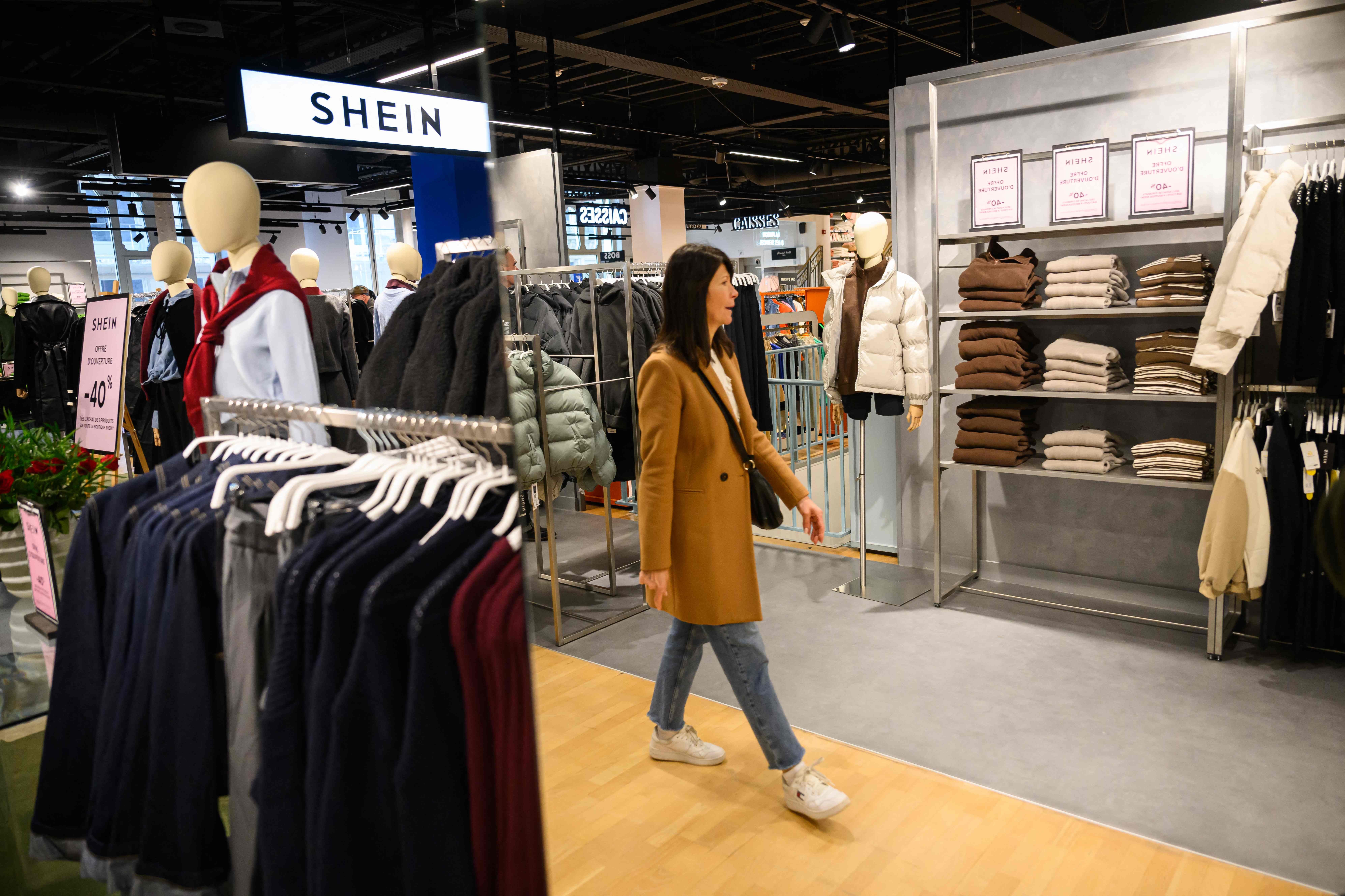 Eine Frau geht durch einen Shein-Store mit Kleidung auf Ständern und Regalen.
