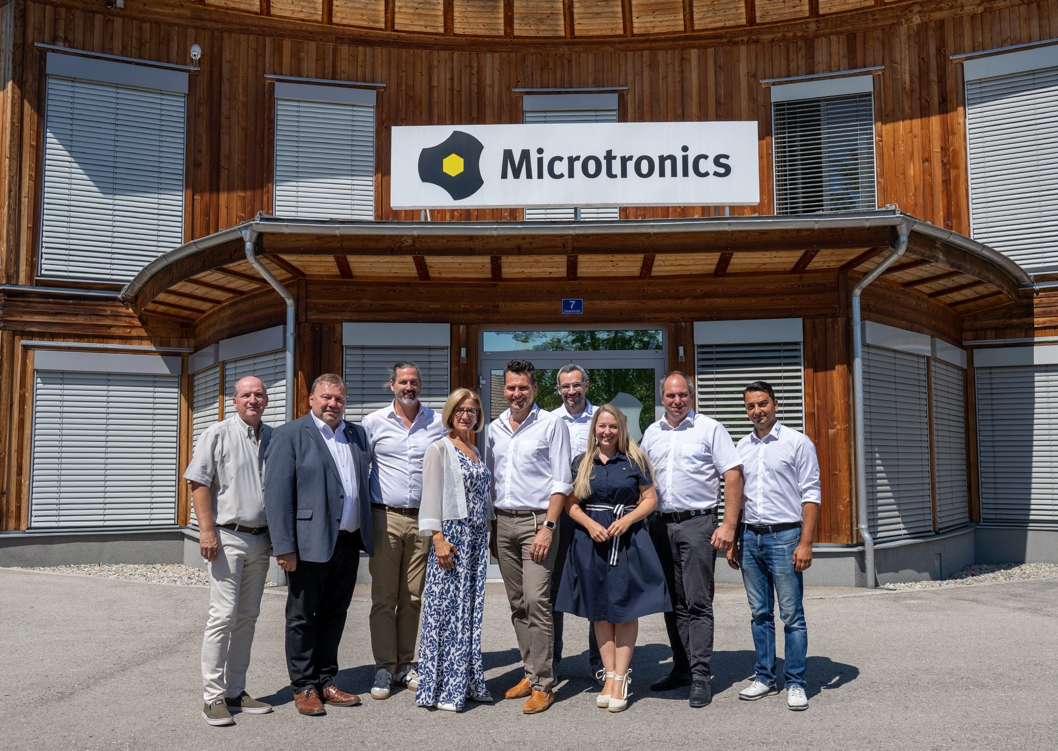 Eine Gruppe von zehn Personen steht vor dem Gebäude von Microtronics und lächelt in die Kamera.