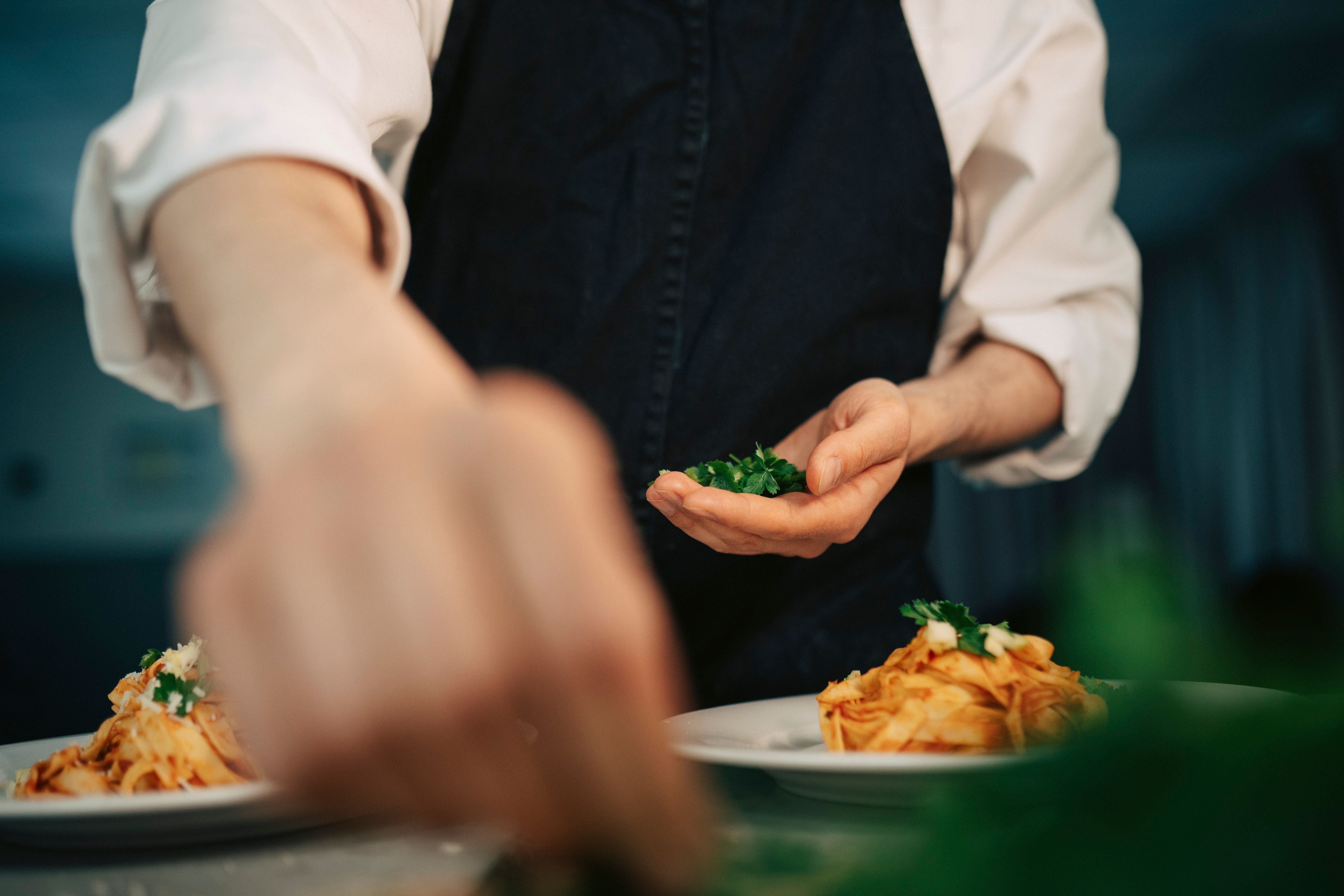 Koch garniert Teller Pasta mit frischen Kräutern.