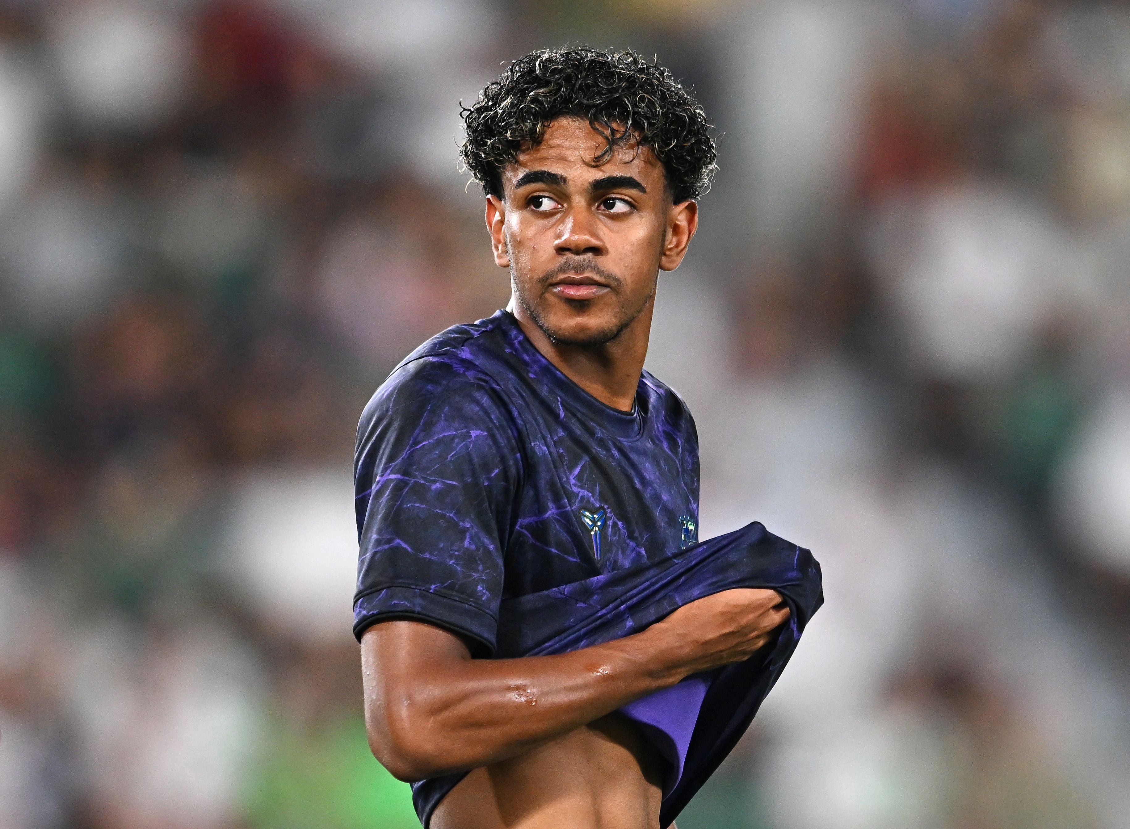 Ein Fußballspieler im Trikot wärmt sich auf und hebt leicht das Shirt, unscharfer Hintergrund.