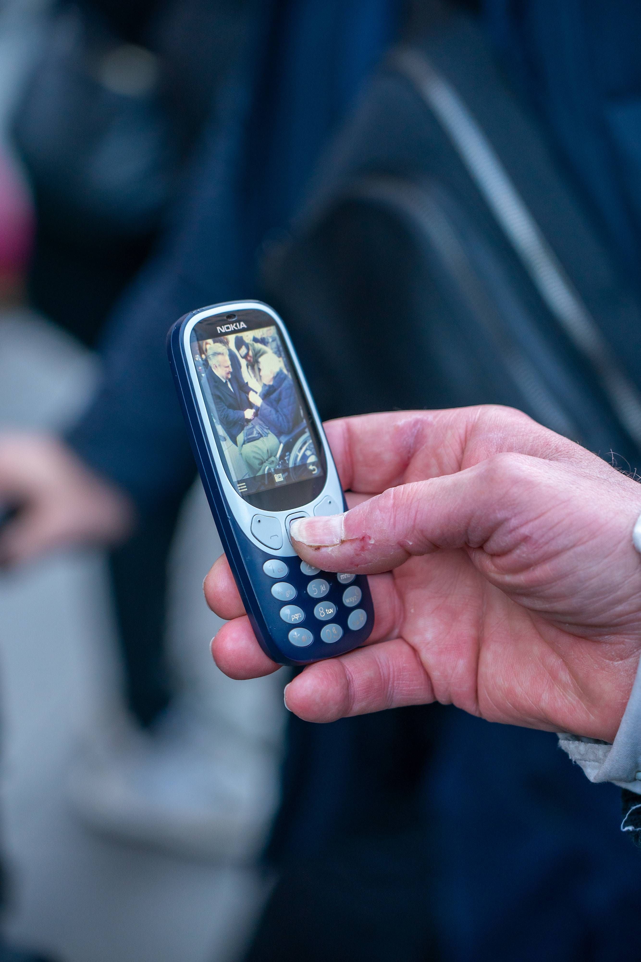 Hand hält ein altes Nokia-Tastenhandy mit Foto auf dem Display bei einer Trauerfeier.
