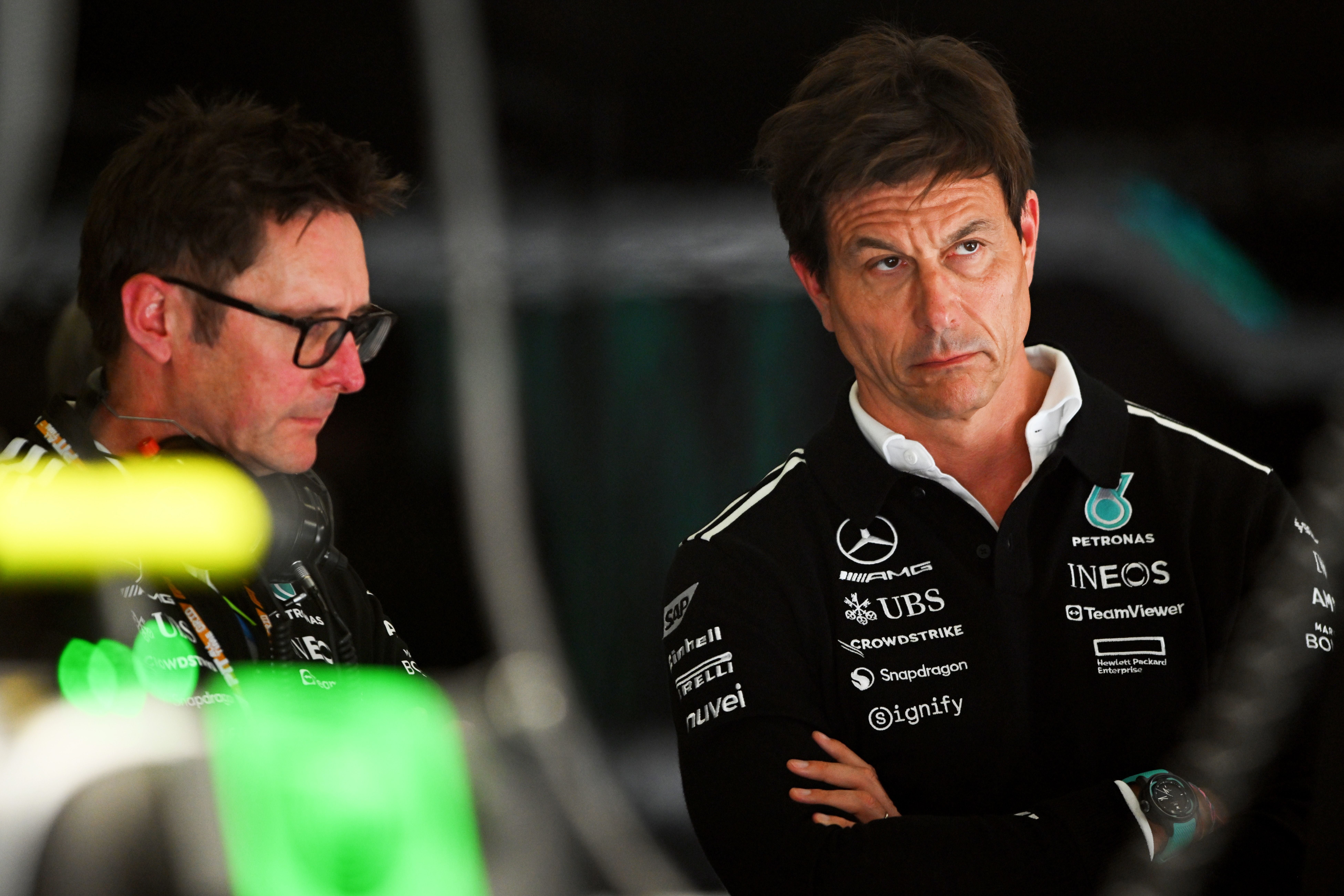 Zwei Männer im Mercedes-Teamoutfit stehen nachdenklich in einer Boxengasse.