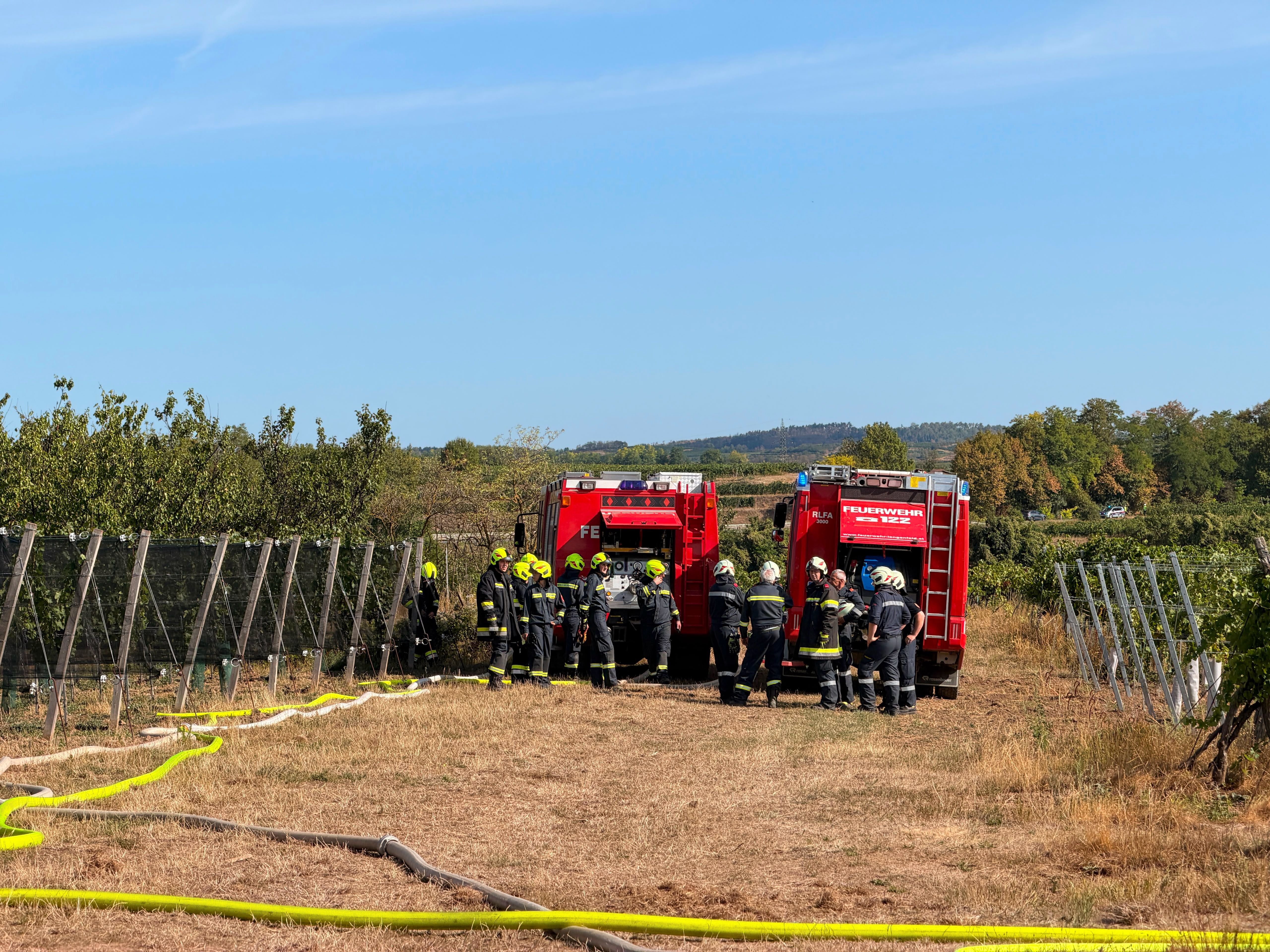 Feuerwehrleute stehen neben zwei roten Einsatzfahrzeugen auf einem Feld bei Krems.