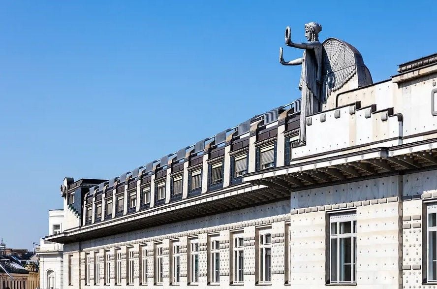 Otto-Wagner-Postsparkasse in Wien mit markanter Engelsstatue auf dem Dach bei blauem Himmel.