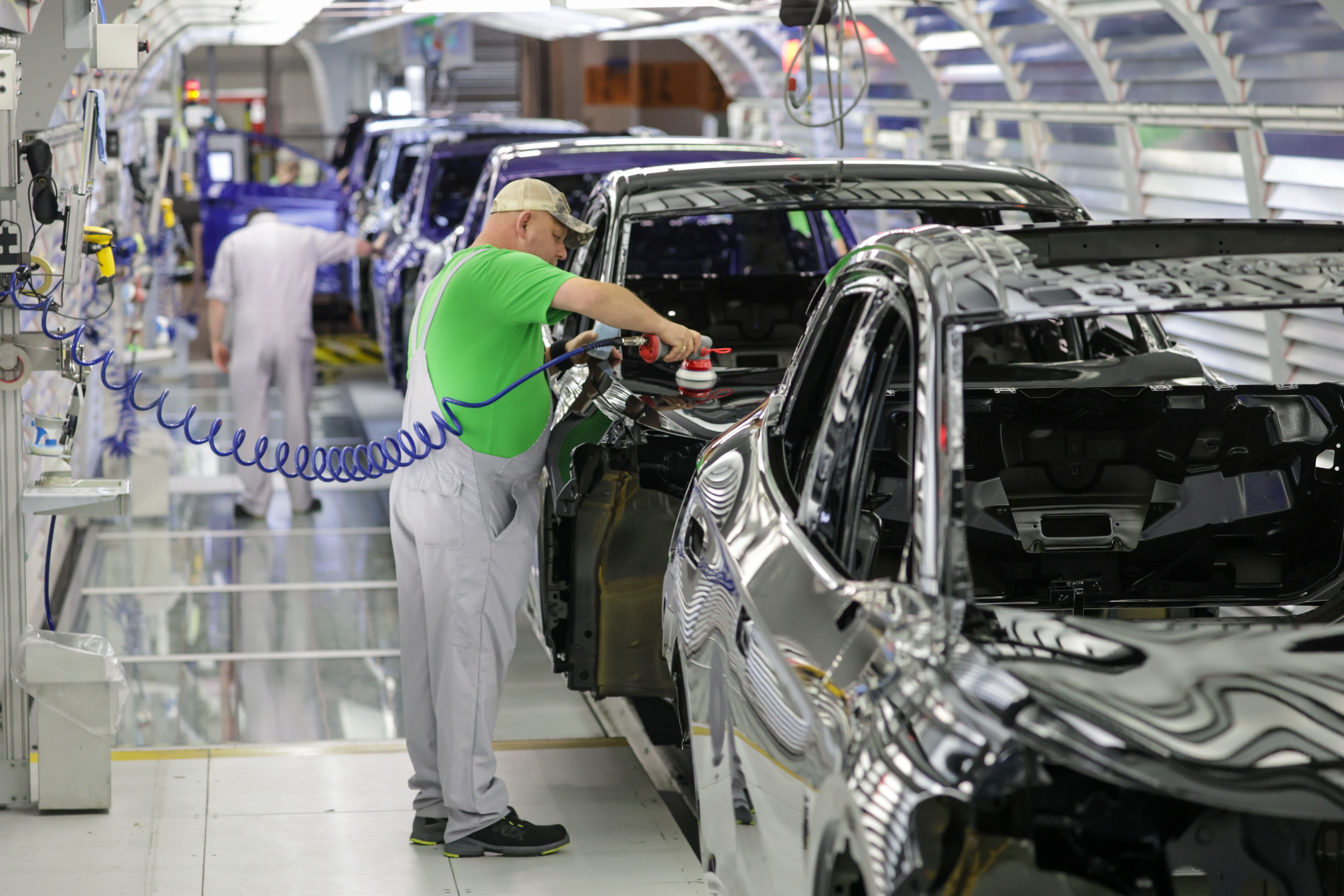 Ein Arbeiter überprüft und poliert Karosserien von Elektroautos in einer Volkswagen-Fabrikhalle.