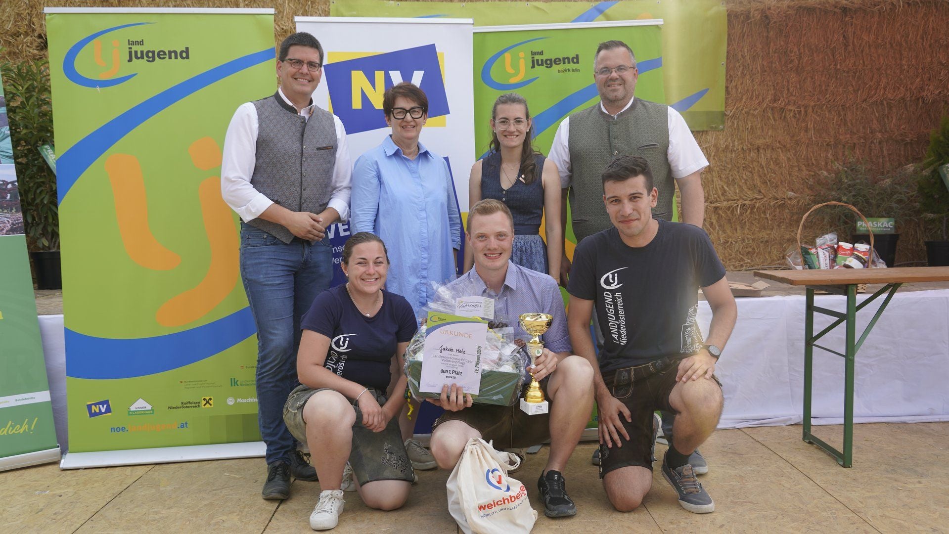 Eine Gruppe von acht Menschen posiert bei einer Siegerehrung mit Urkunde und Pokal.